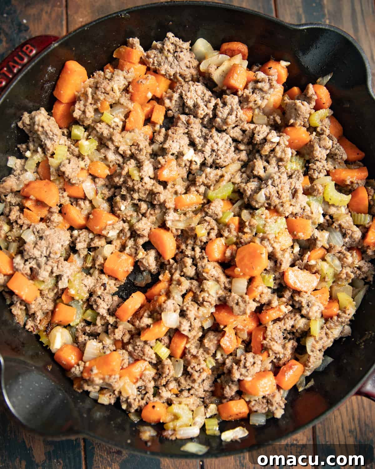 Ground beef with carrots and celery in a cast iron skillet.