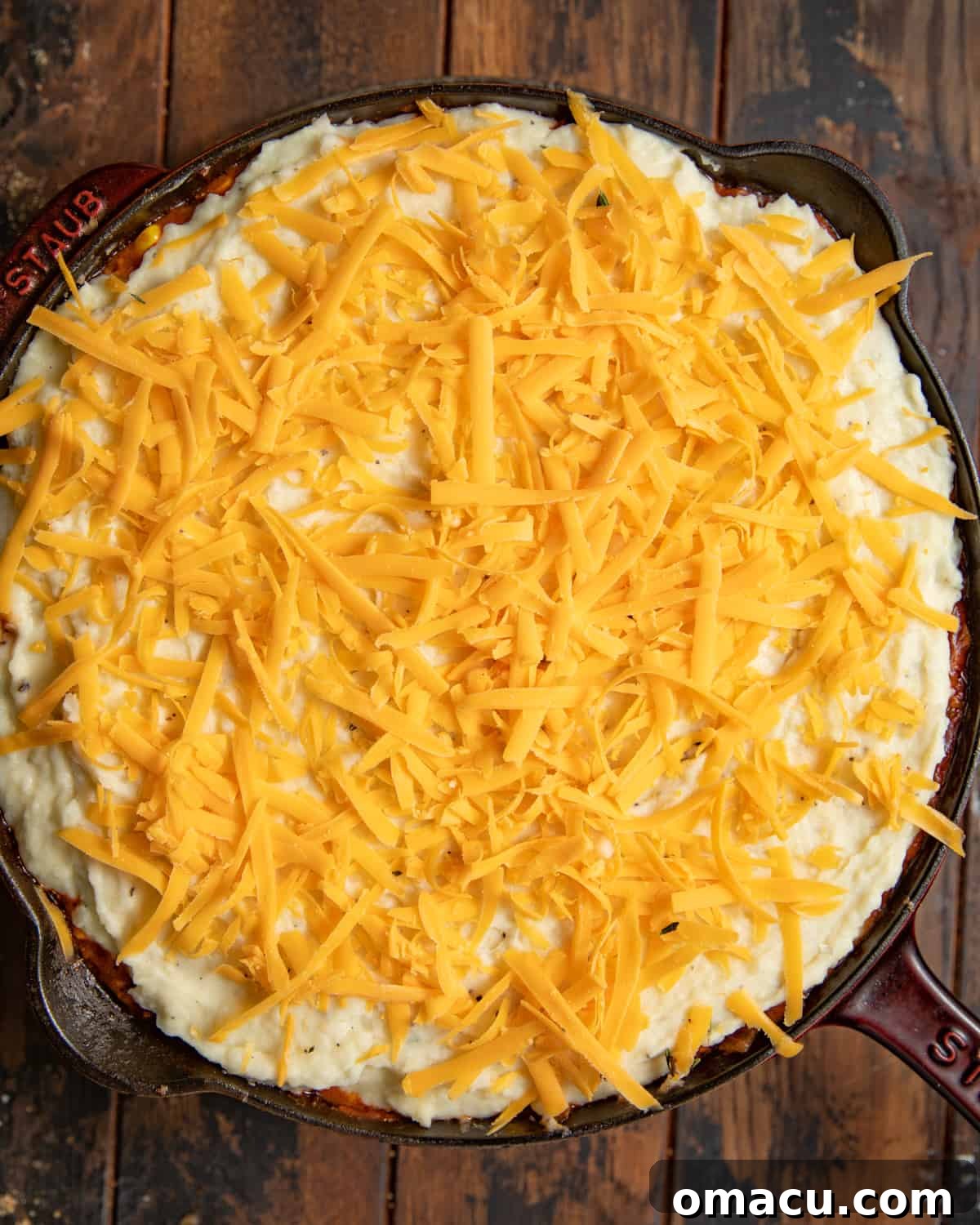 Mashed potatoes and shredded cheddar over shepherd's pie filling in a cast iron skillet.