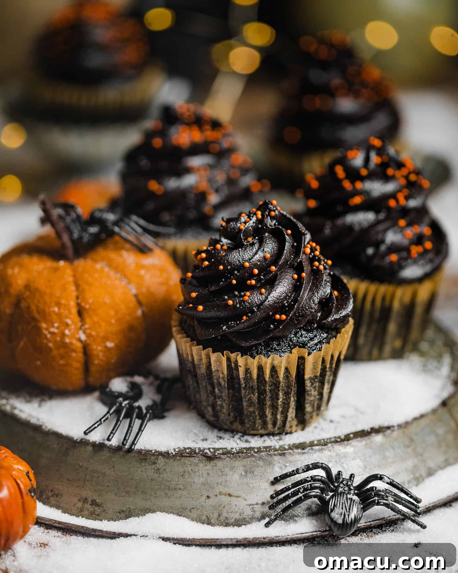 Cupcakes on a silver platter with a pumpkin and lights in the background, creating a festive ambiance.