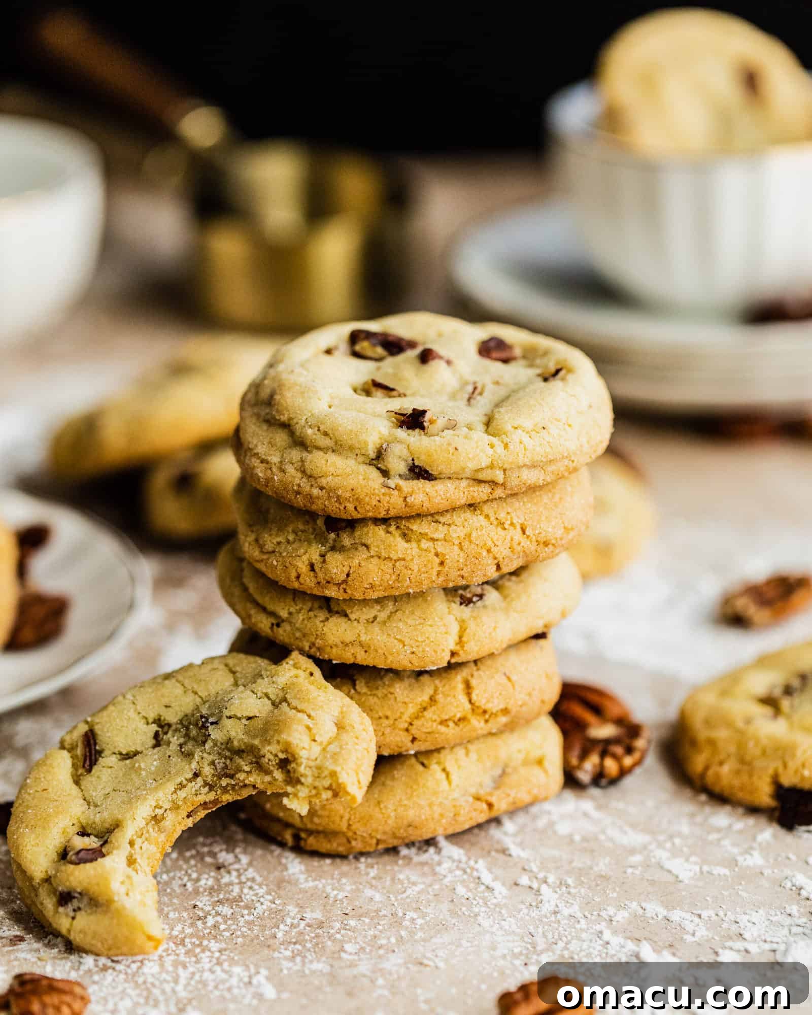 A stack of Vanilla Bean Butter Pecan Cookies, with more cookies scattered around, highlighting their golden brown exterior.