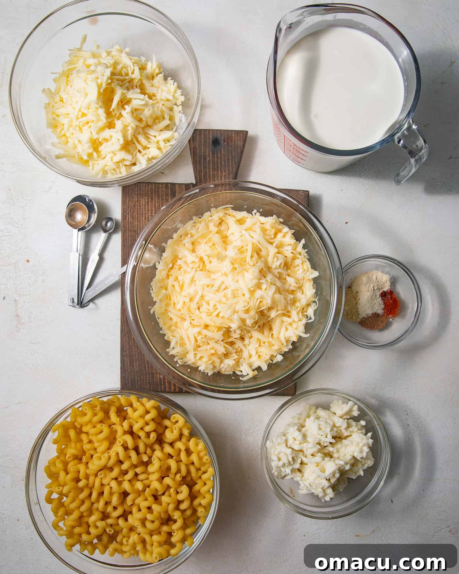 A visually appealing flat lay of all the essential ingredients needed to create smoked gouda mac and cheese, including heavy cream, milk, a selection of spices (thyme, nutmeg, cayenne pepper, smoked paprika, garlic powder, onion powder, ground mustard), blocks of mozzarella, sharp cheddar, and smoked gouda cheese, all-purpose flour, butter, and dry pasta.