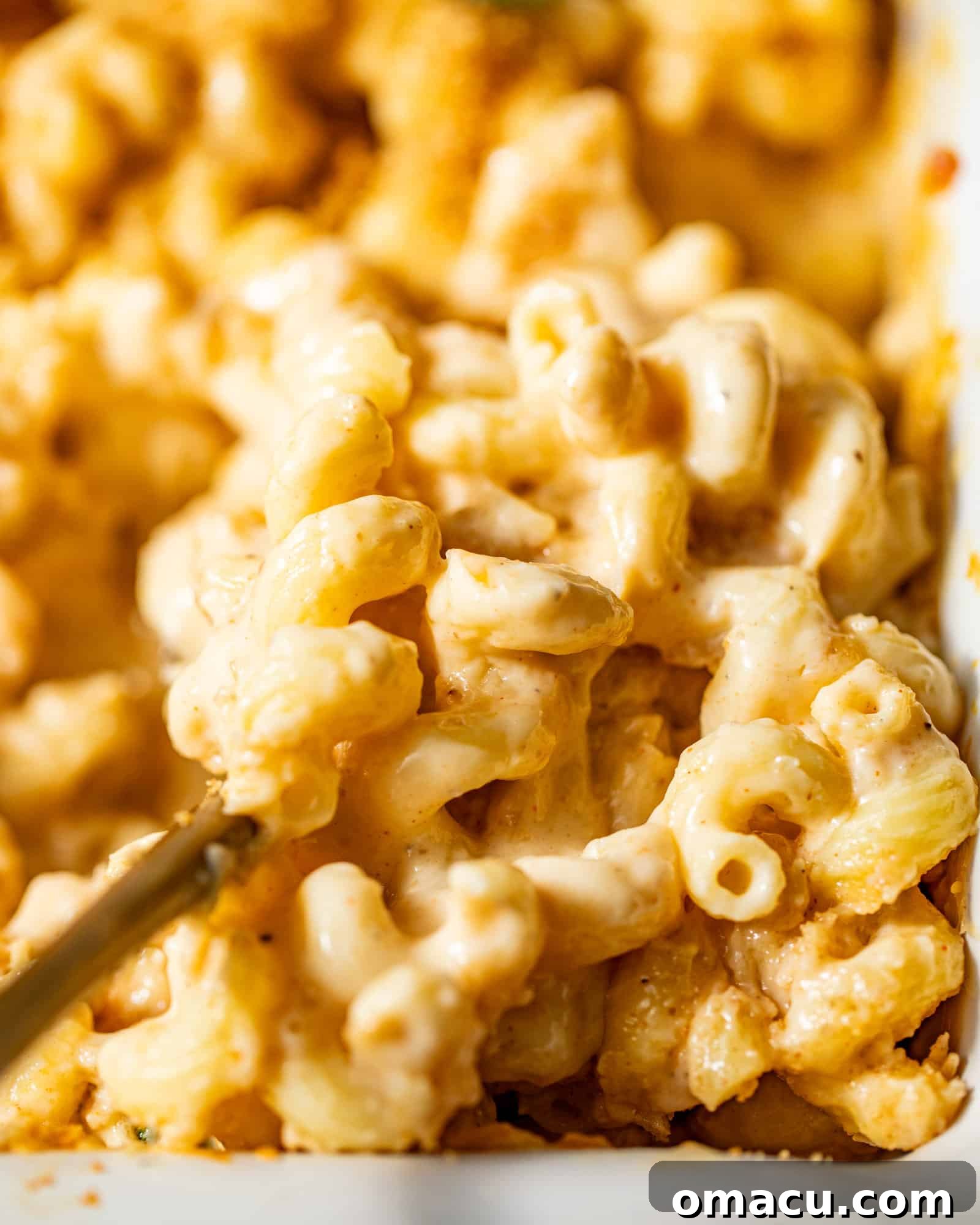 A close-up photograph of creamy, golden-baked macaroni and cheese in a rustic dish, showcasing its rich, bubbly texture and tantalizing golden crust, inviting you to take a scoop.
