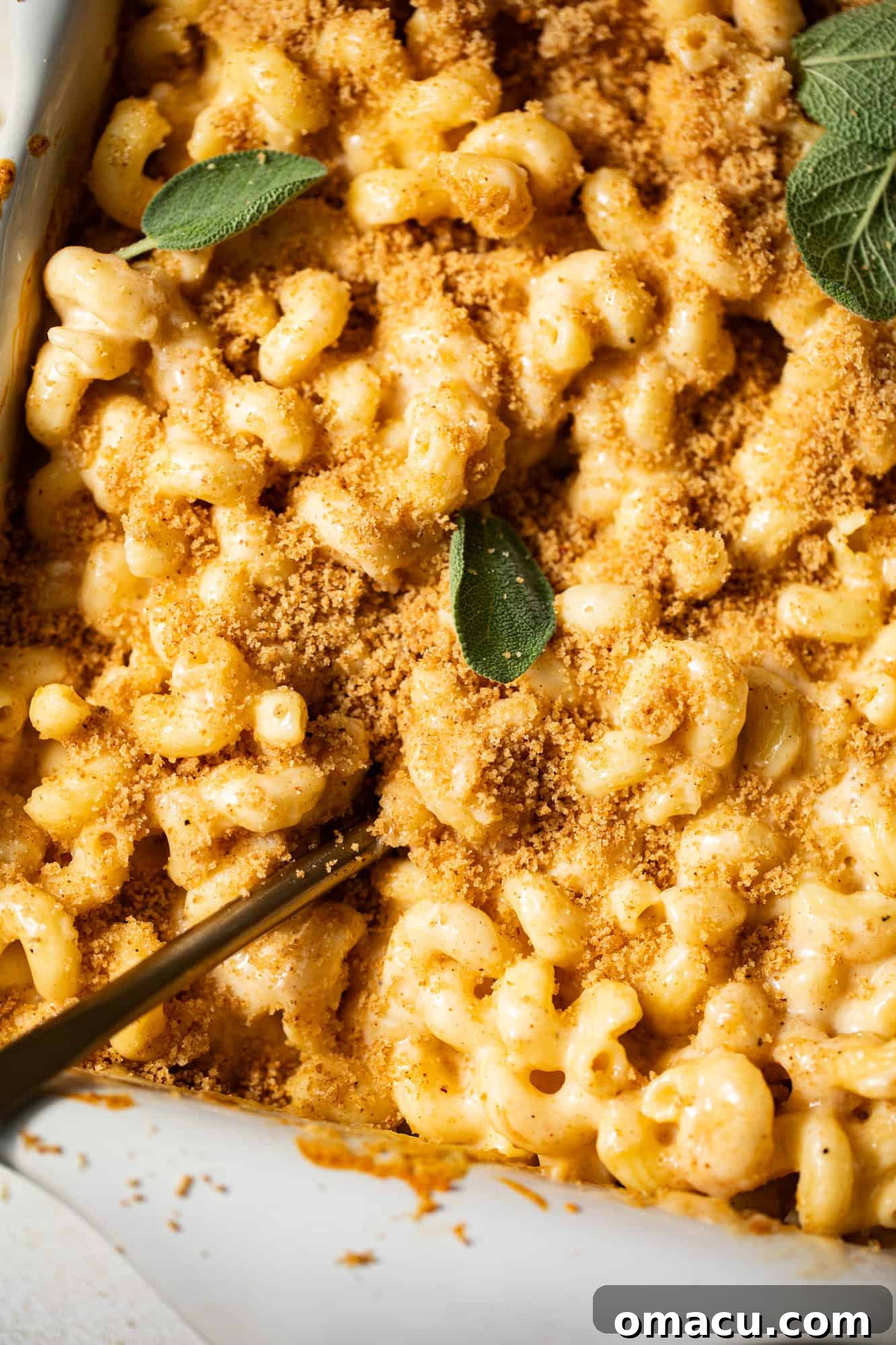 A serving spoon expertly lifting a generous portion of creamy, baked smoked gouda mac and cheese from a 9x13 inch baking dish, showcasing its perfect gooey texture and golden topping.