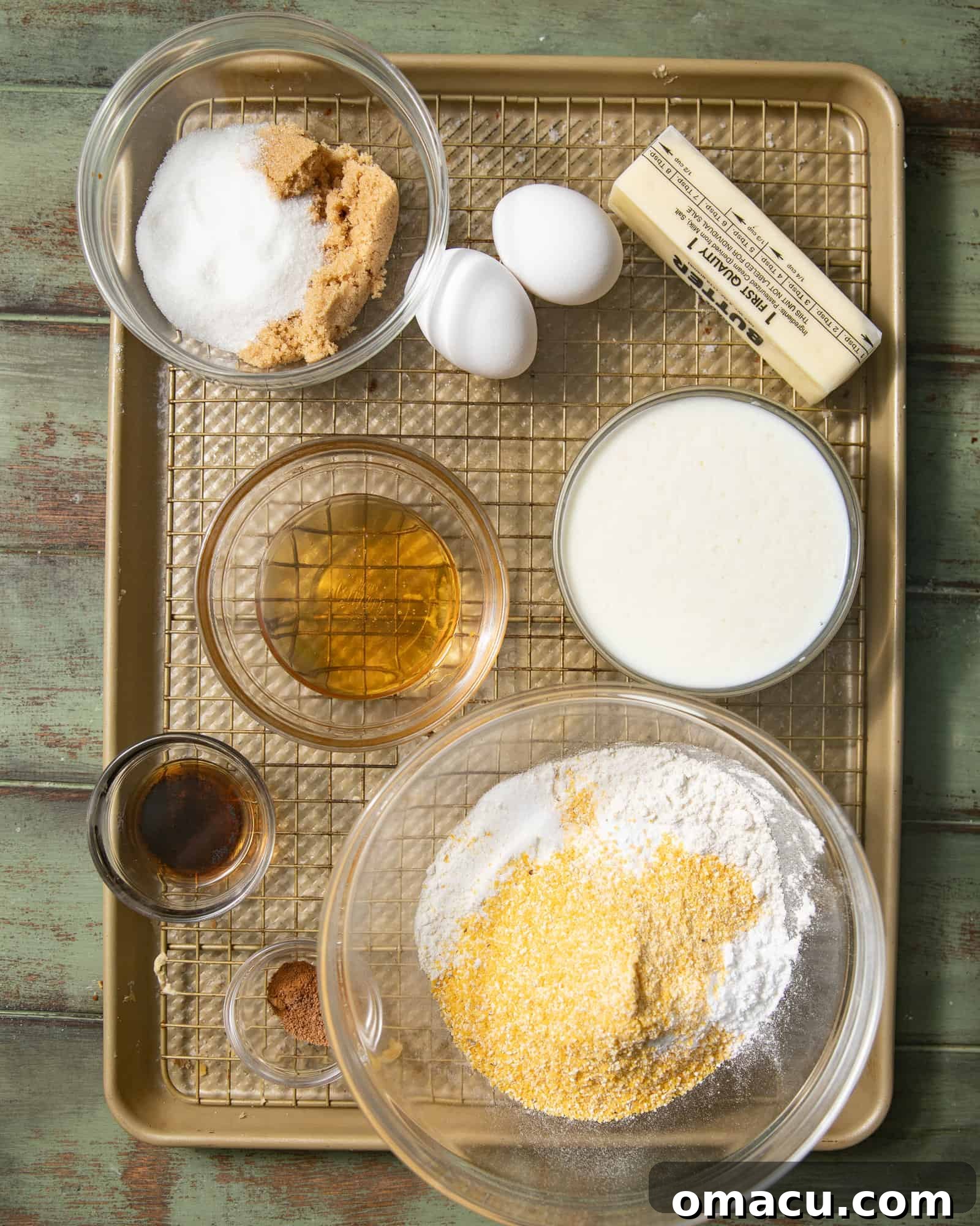 Small bowls containing honey butter cornbread ingredients: butter, sugar, brown sugar, honey, cornmeal, flour, vanilla extract, eggs, and buttermilk.