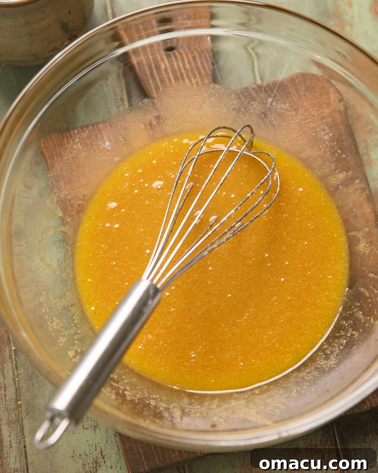 Melted honey, butter, sugar, and brown sugar whisked together in a clear glass mixing bowl.