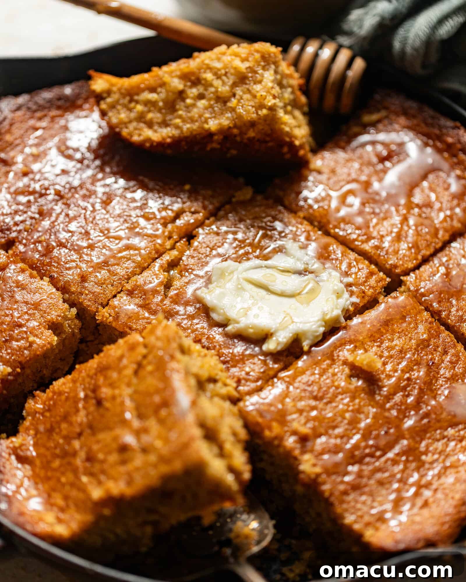 Honey butter cornbread in a cast iron skillet, topped with melted honey butter and a drizzle of extra honey.