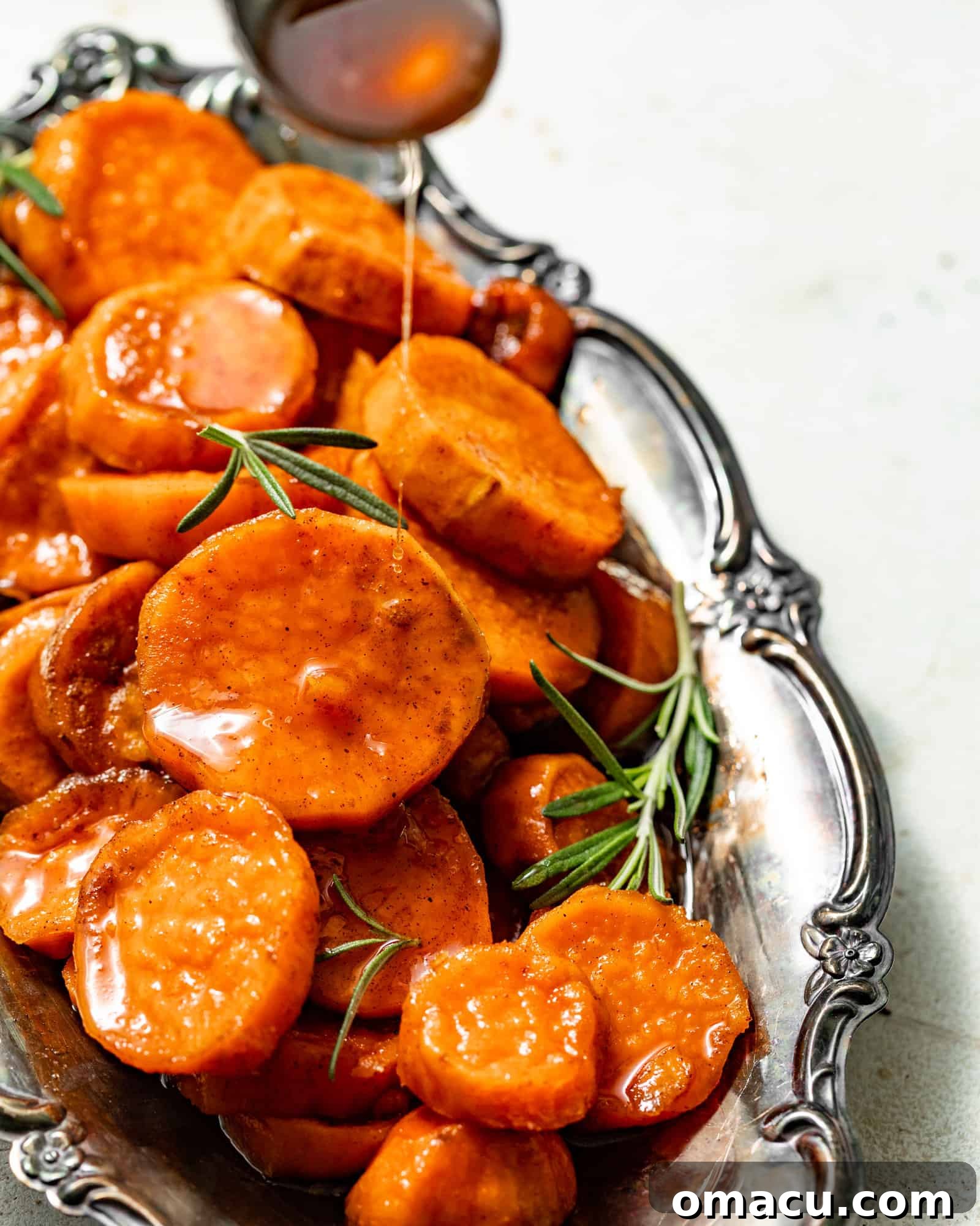 A spoon generously pouring rich, thick syrup over a serving of stovetop candied yams, highlighting their glossy finish.