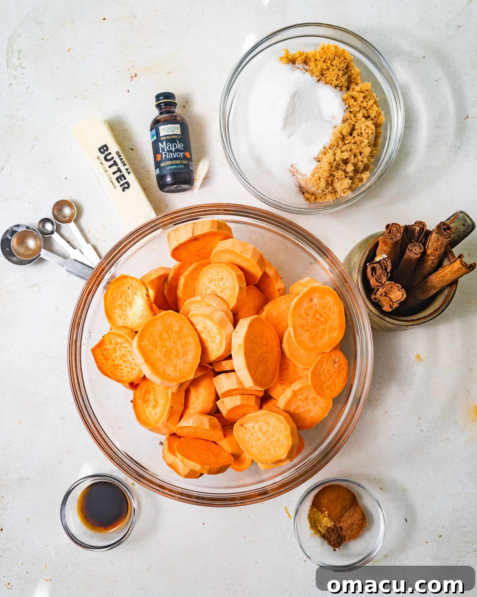 A vibrant flat lay photo showcasing all the fresh ingredients needed for homemade candied yams: sweet potatoes, butter, brown sugar, white sugar, vanilla extract, maple extract, cinnamon, salt, nutmeg, and ginger.