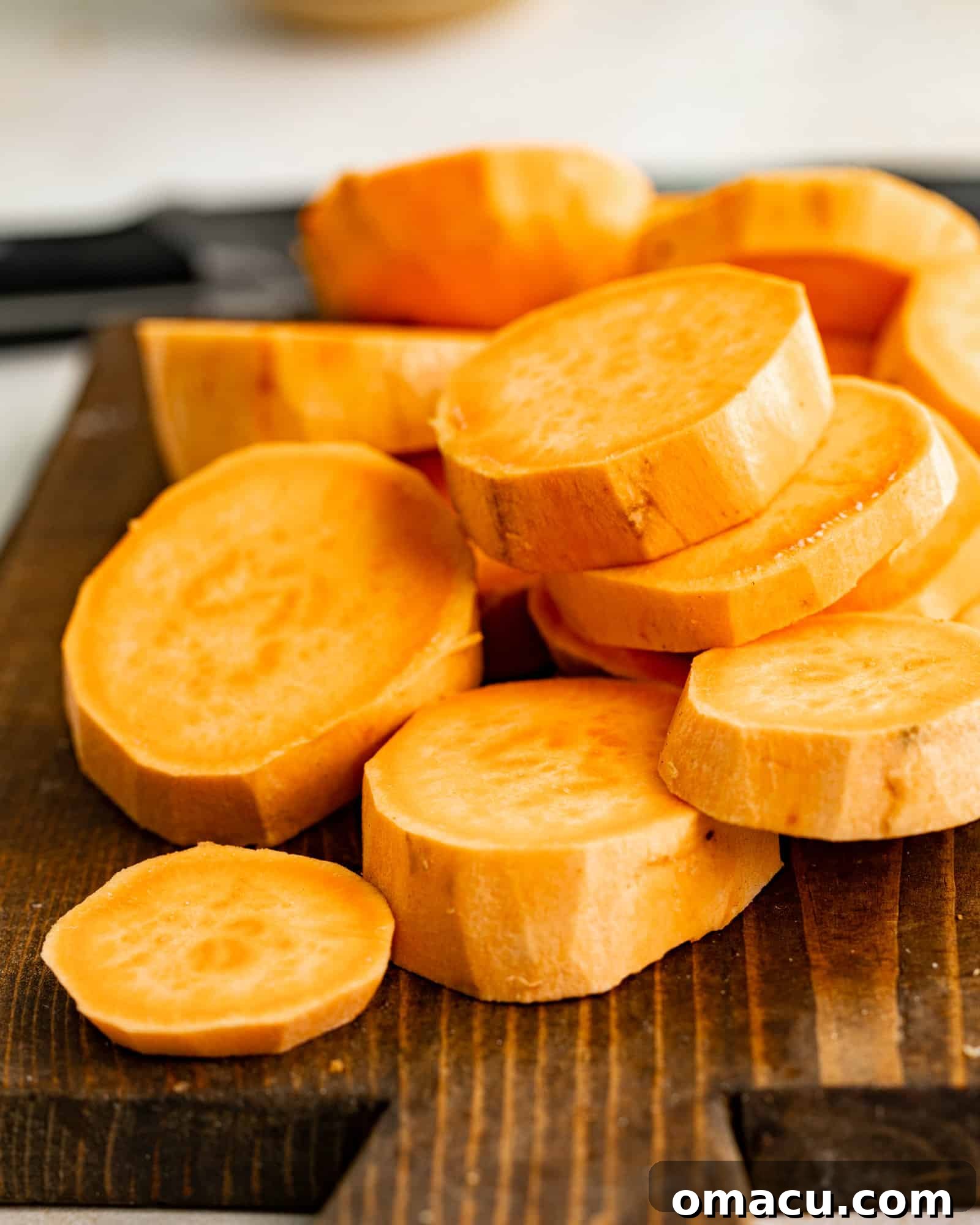 Peeled and uniformly sliced sweet potatoes resting on a cutting board, ready for cooking.