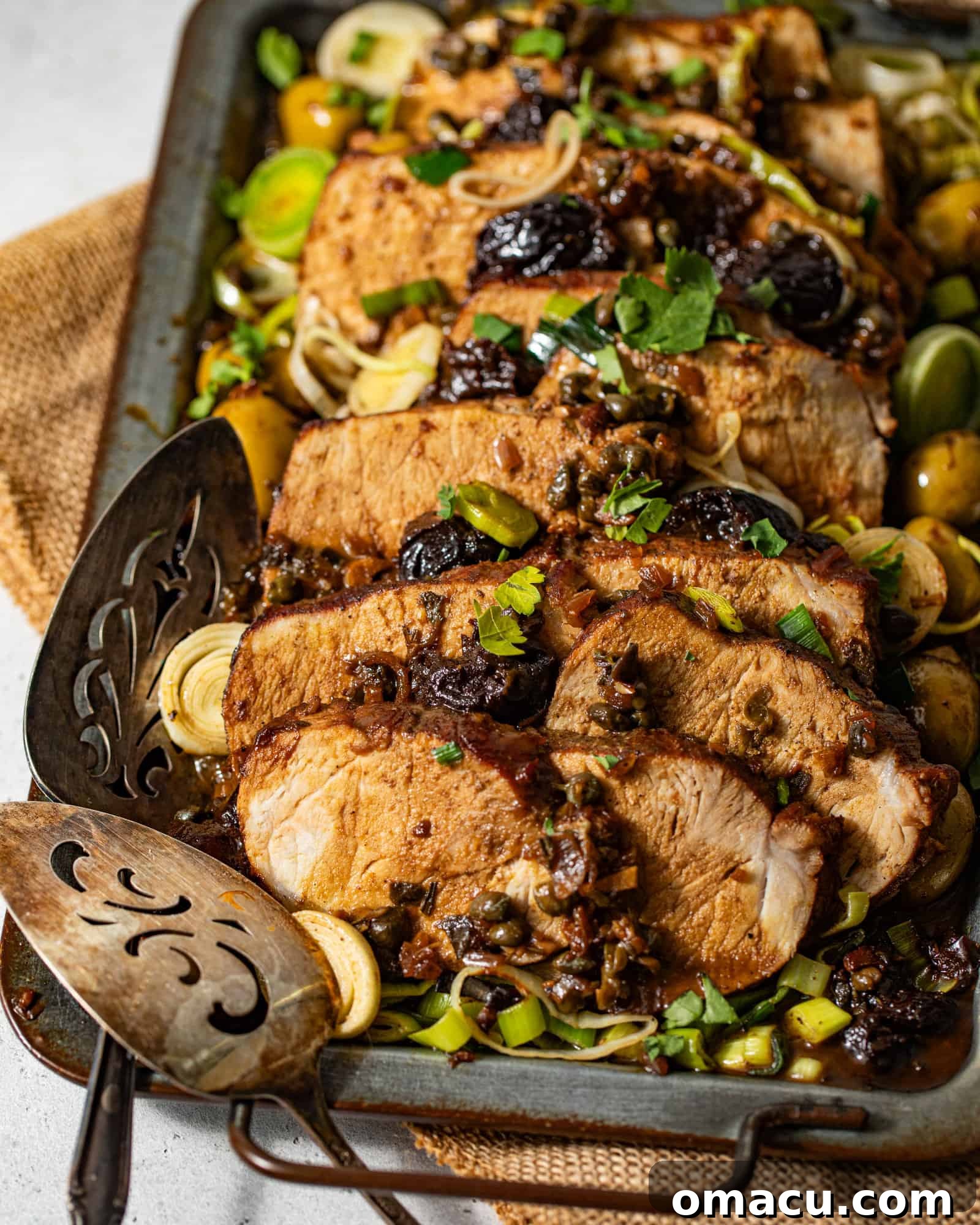 Pork Marbella served elegantly on a platter, garnished with prunes, capers, leeks, and green olives.