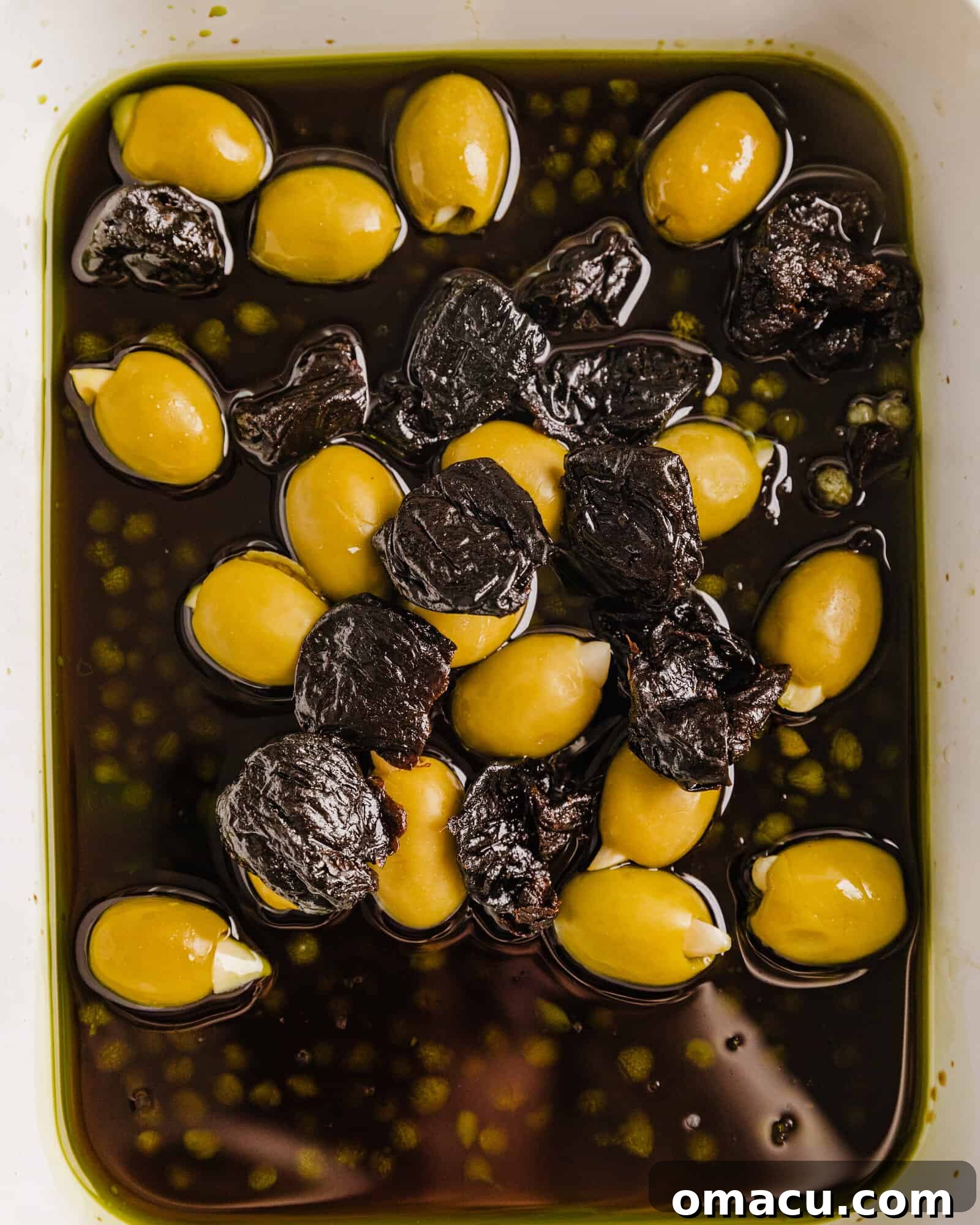 A close-up shot of a bowl filled with the Pork Marbella marinade ingredients: green olives, prunes, balsamic vinegar, and olive oil, ready for the pork tenderloin.