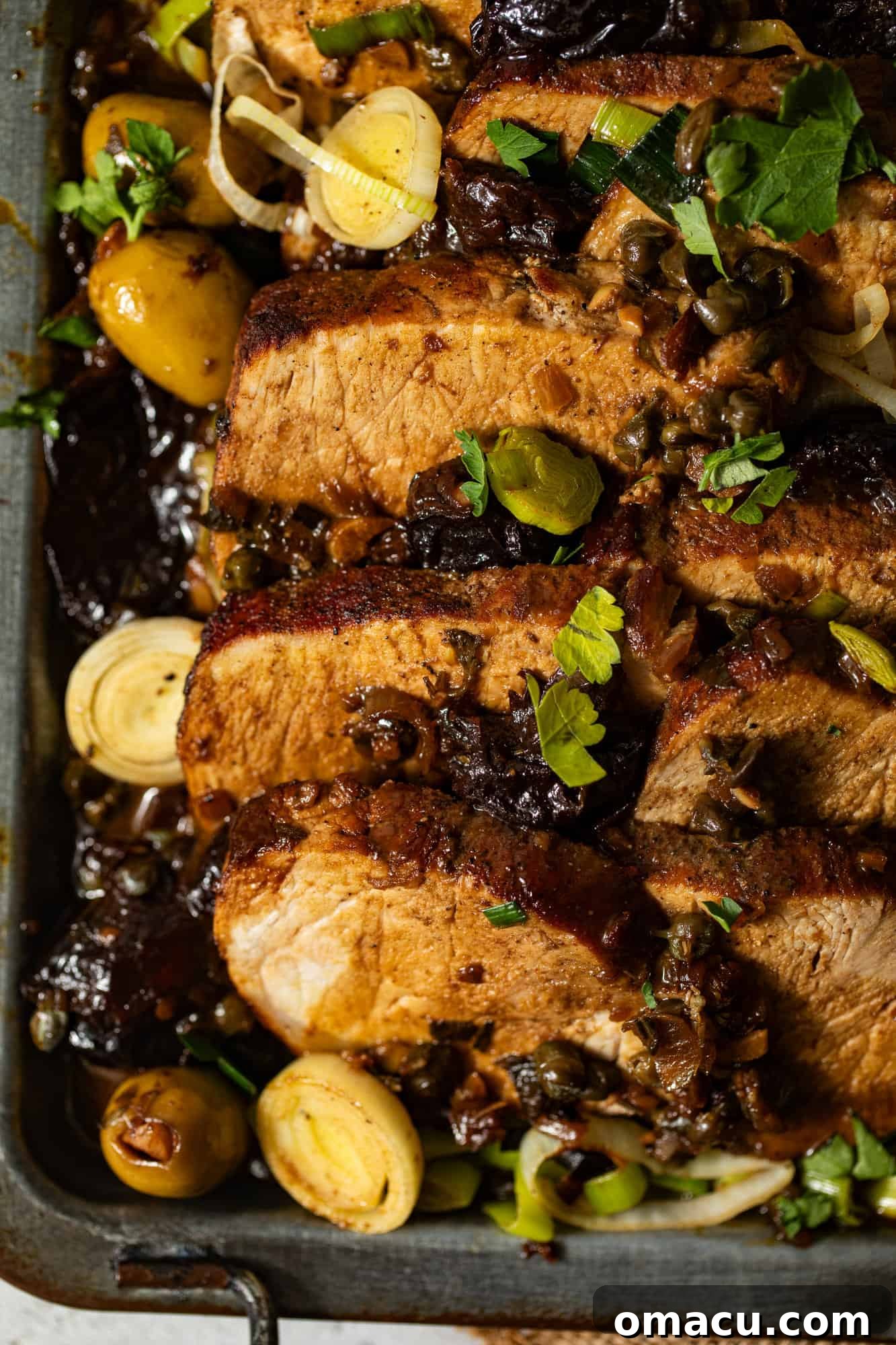 An overhead view of the finished Pork Marbella dish on a serving platter, showcasing the rich sauce, tender pork, prunes, olives, and capers.