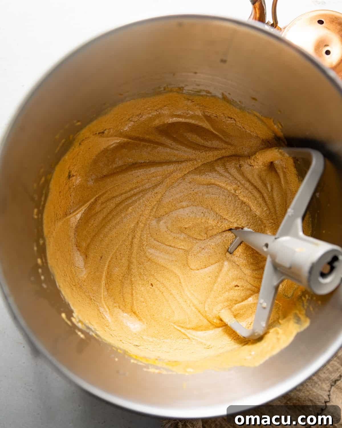 Wet ingredients like butter, oil, and dark brown sugar are being creamed together in the bowl of a stand mixer using the paddle attachment until light and fluffy.