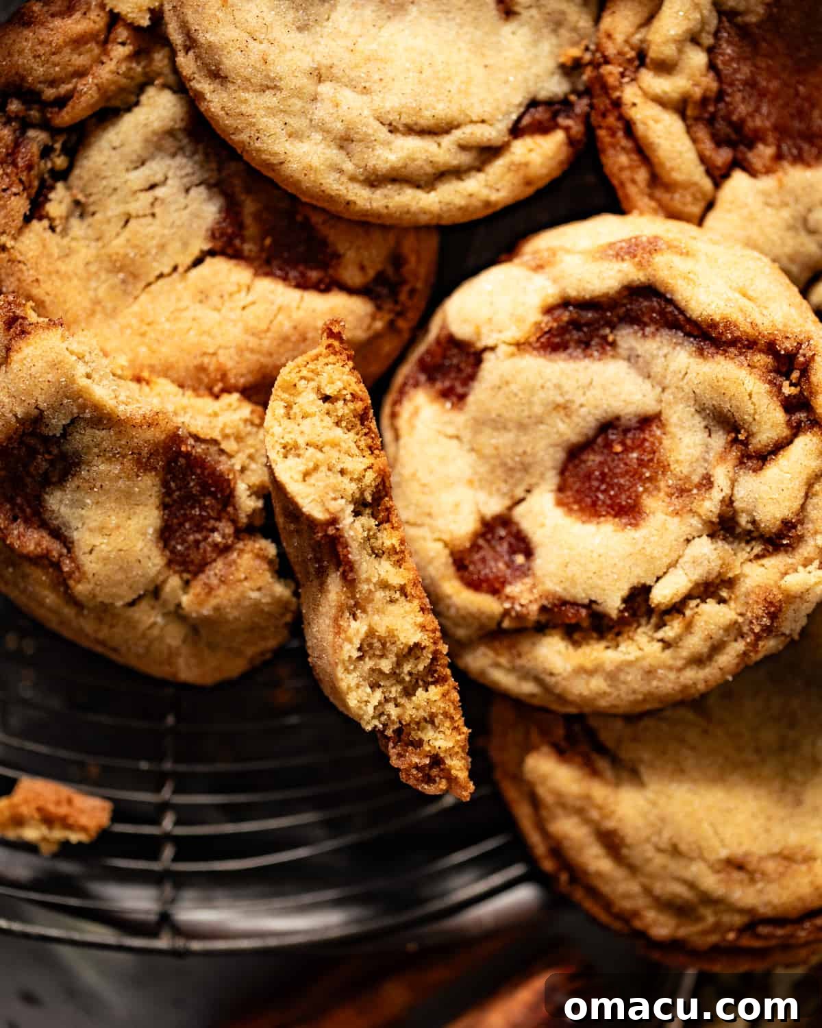 Close-up of cinnamon roll cookies on a wire rack, with one cookie cut in half to show the cinnamon swirl filling