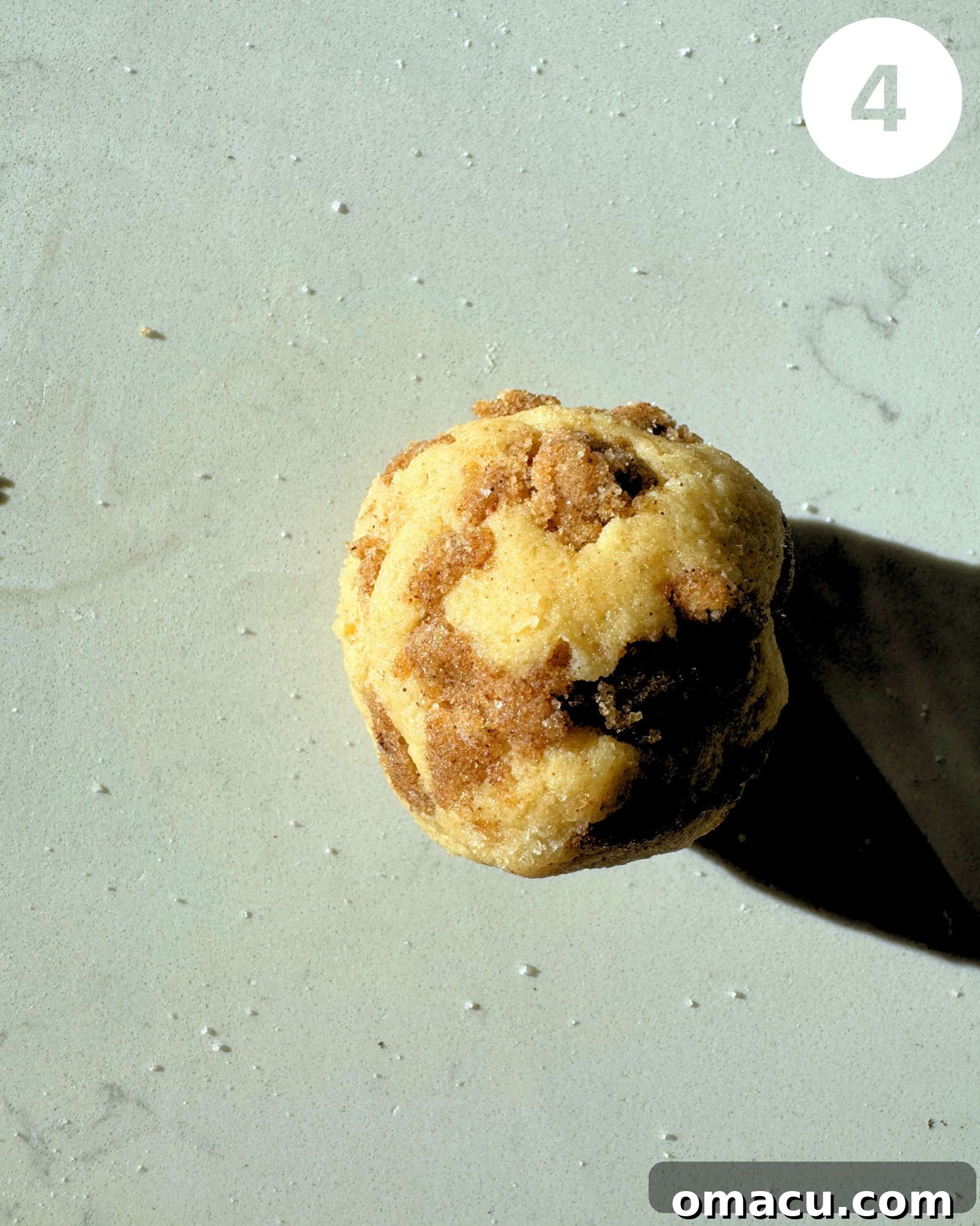A perfectly rolled cookie dough ball, coated in cinnamon sugar, ready for baking on a white surface