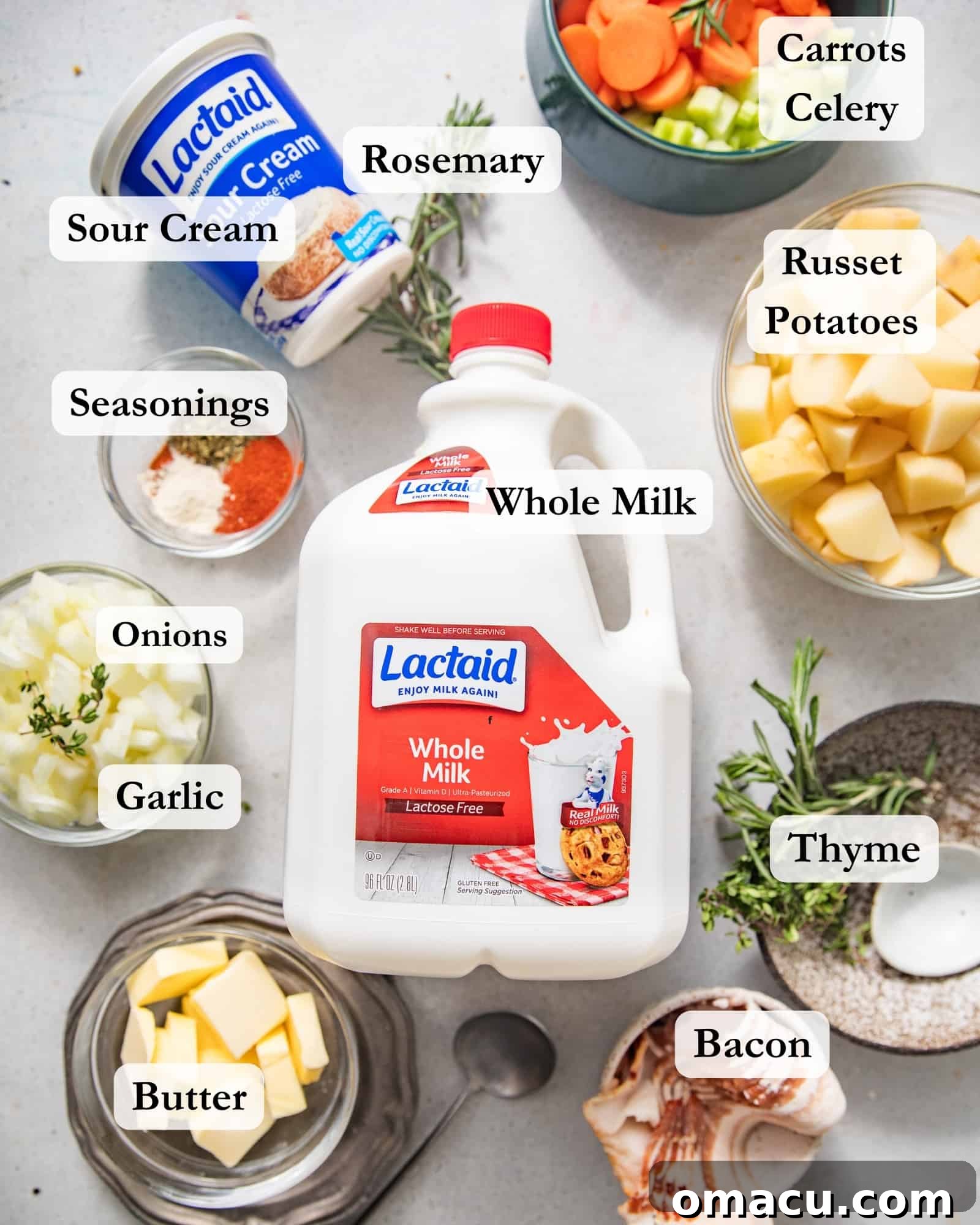 ingredients to make loaded baked potato soup on a white surface - russet potato, whole milk, bacon, butter, celery, carrots, thyme, rosemary, seasonings, onions, garlic, sour cream, and chicken bouillon paste.