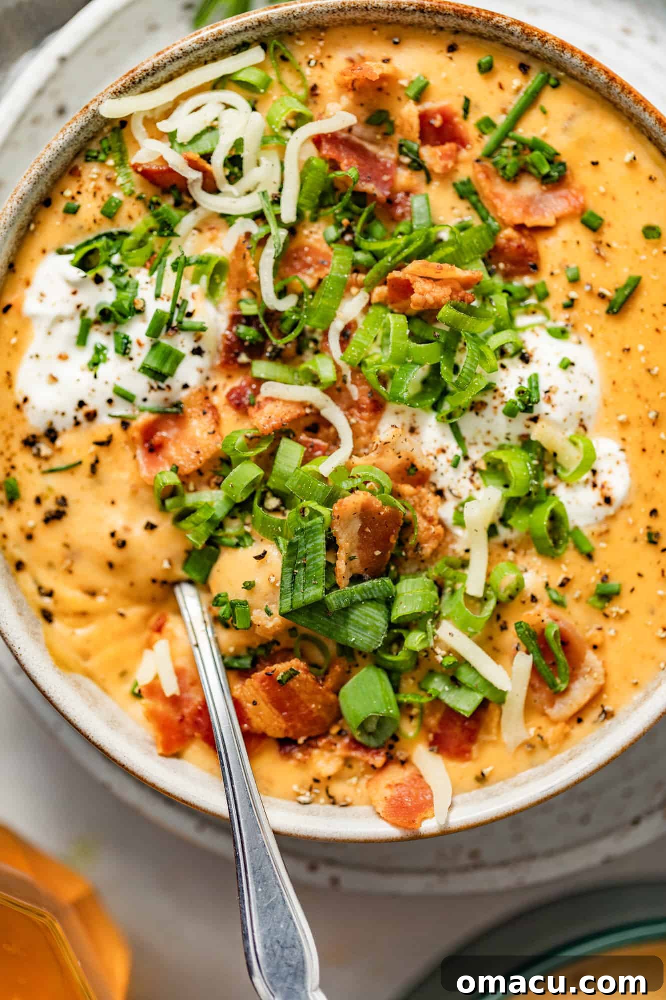 loaded baked potato soup in a bowl with a spoon and topped with crispy bacon, green onions, chives, cheddar cheese, and sour cream