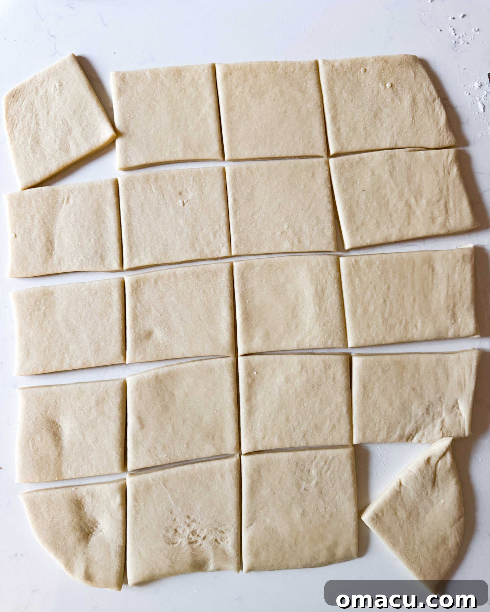 Beignet dough cut into 3 inch squares on a white surface