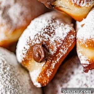 Up close photo of Nutella beignets topped with powdered sugar and Nutella coming out of the beignet.