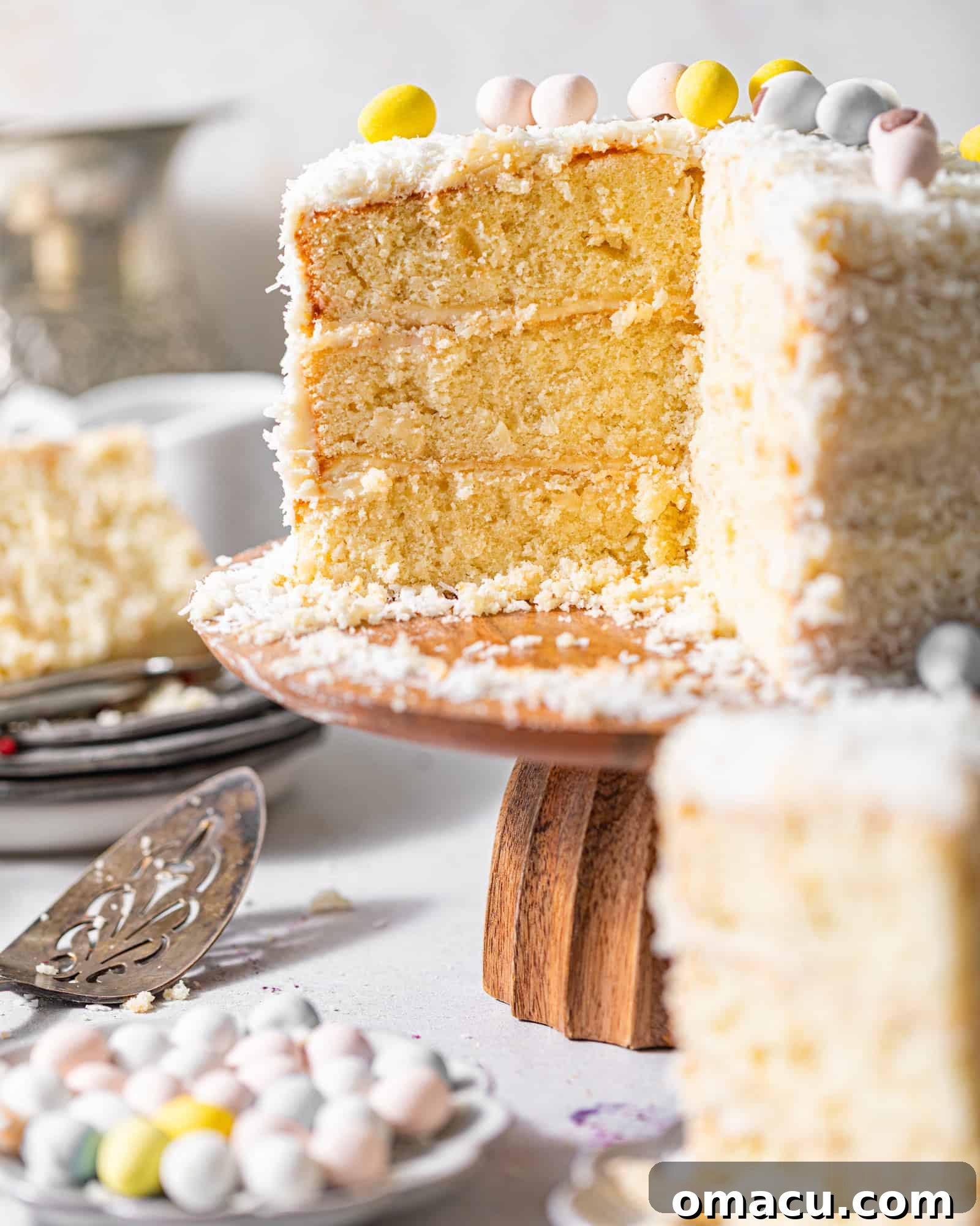 A beautifully decorated coconut cake on a cake stand, topped with mini Cadbury eggs and coated in coconut shreds.