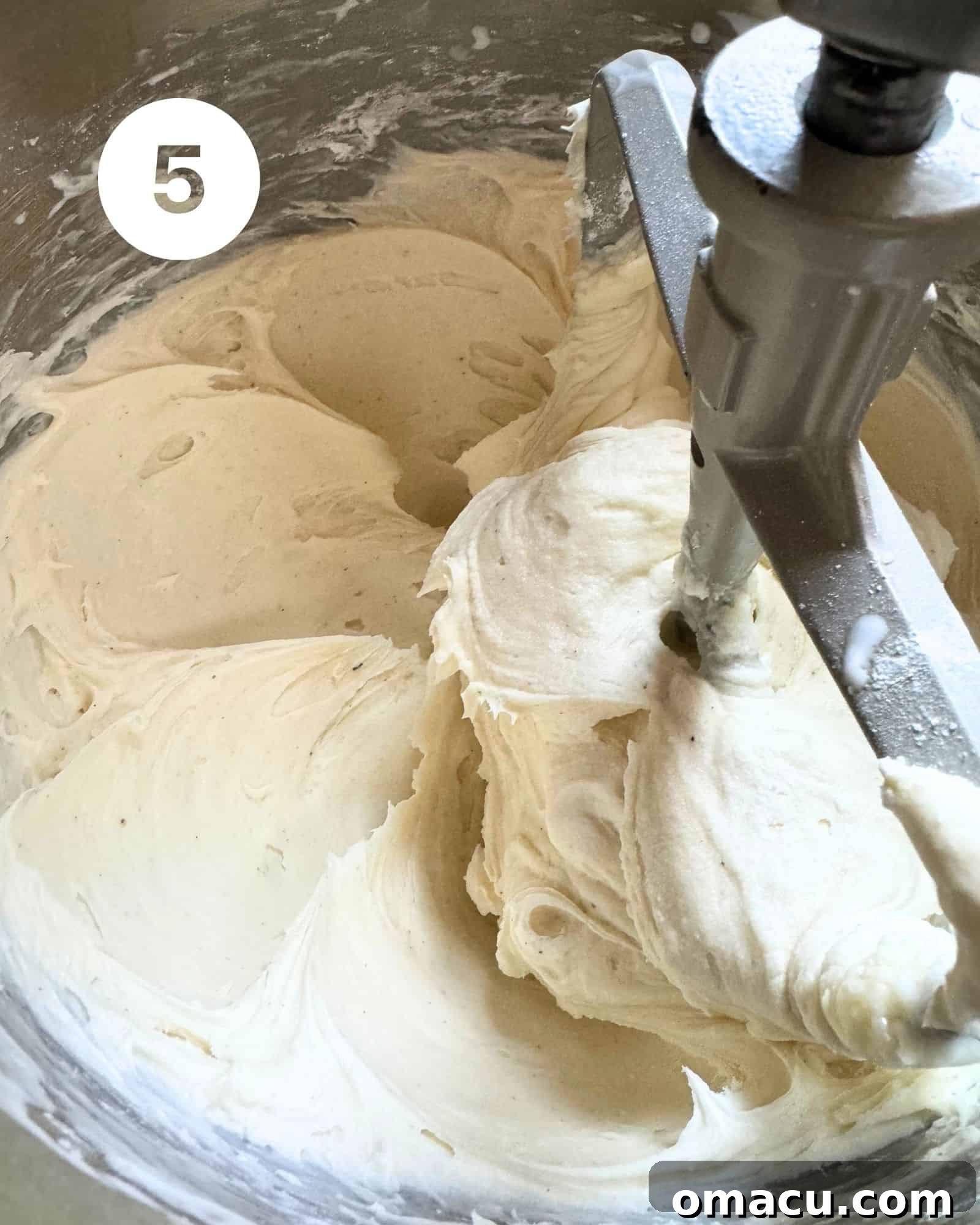 Coconut cream cheese frosting in the bowl of a stand mixer fitted with the paddle attachment, showing its smooth and creamy texture.