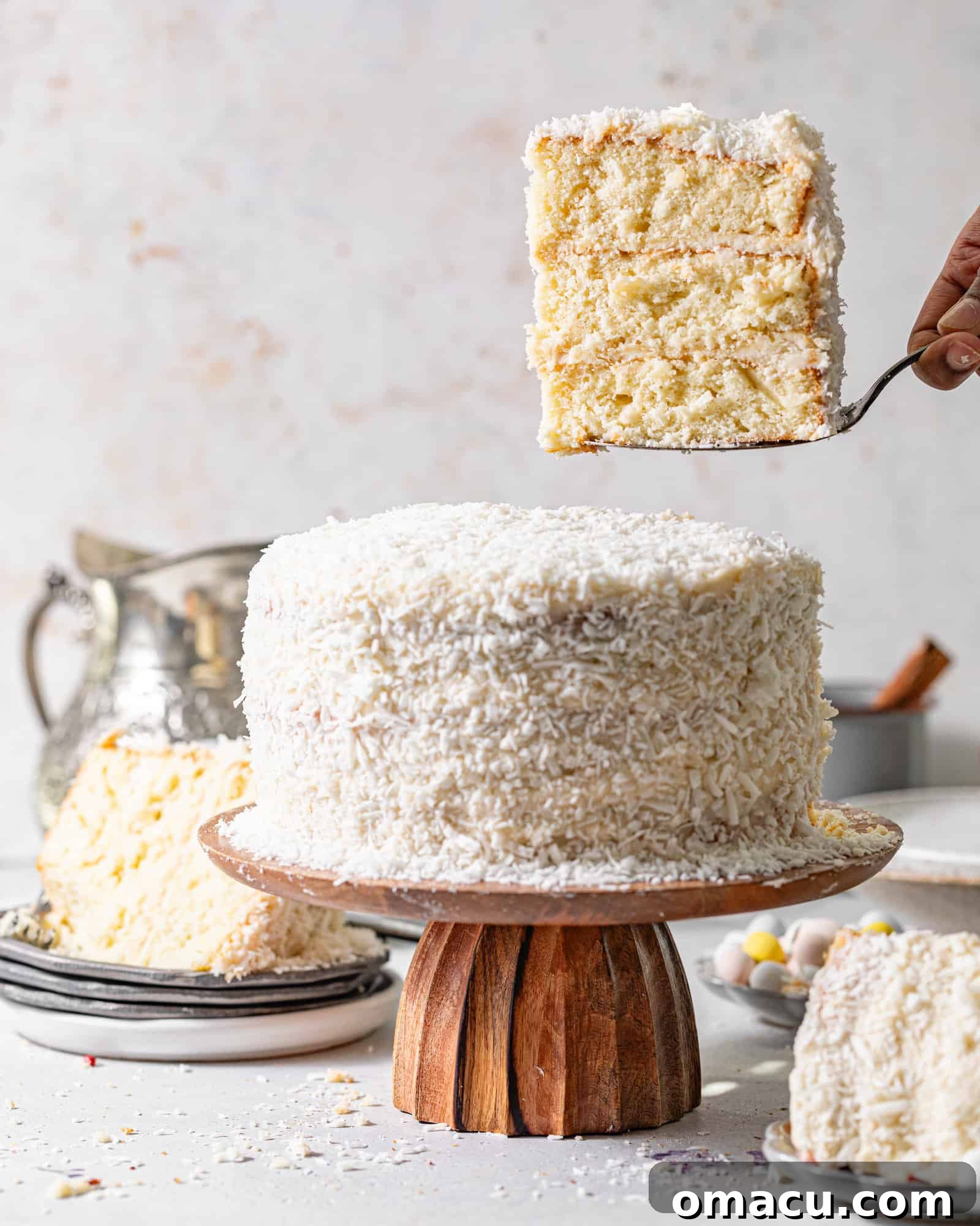 A delectable slice of coconut cake being carefully lifted from the cake stand with a cake server, showcasing its layers and rich frosting.