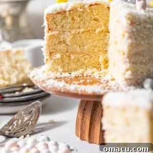 A beautifully decorated coconut cake on a cake stand, topped with mini Cadbury eggs and coated in coconut shreds.