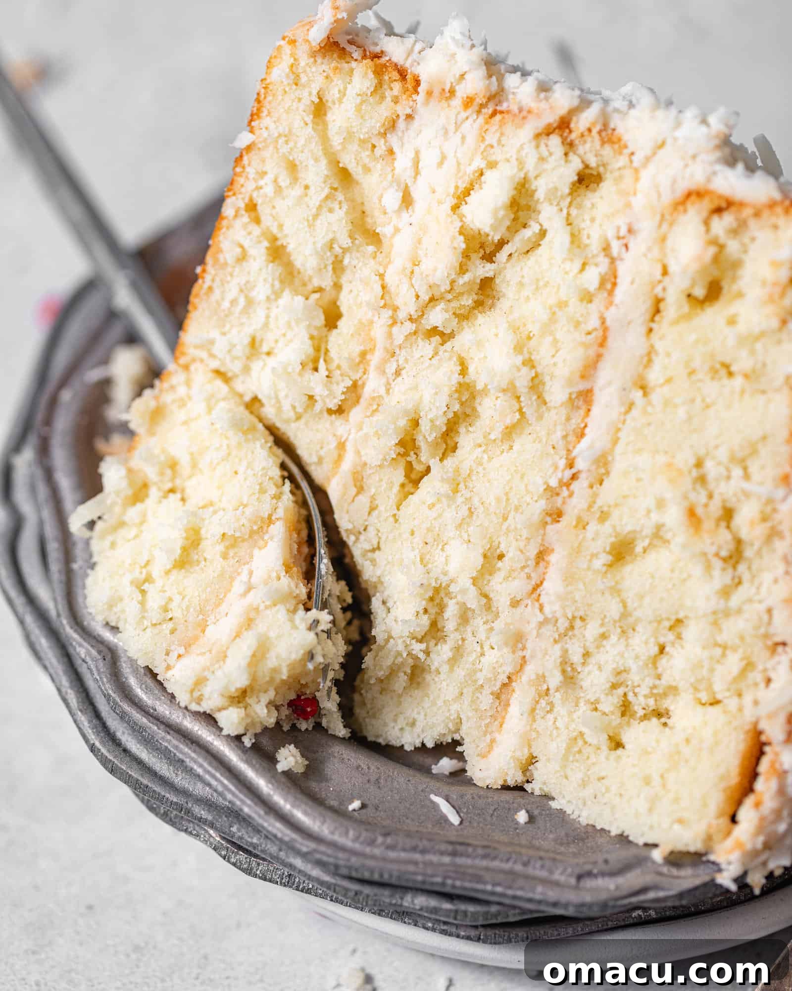 A tempting slice of coconut cake resting on a elegant silver plate, accompanied by a fork, ready to be enjoyed.