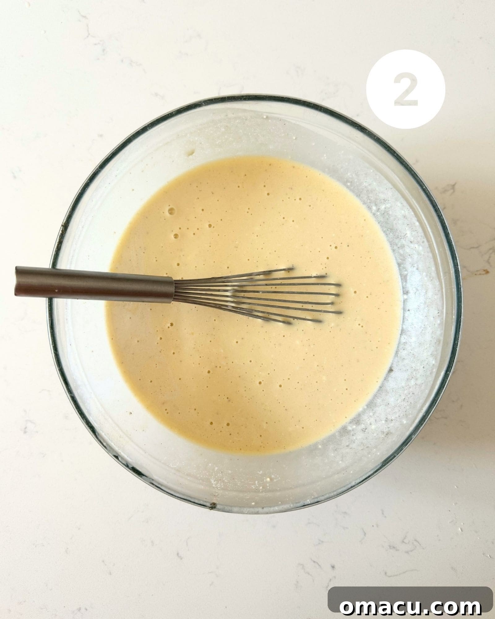 Vegetable oil, sour cream, eggs, canned coconut milk, coconut emulsion, and vanilla bean paste whisked together in a large mixing bowl, illustrating the smoothly combined wet ingredients.