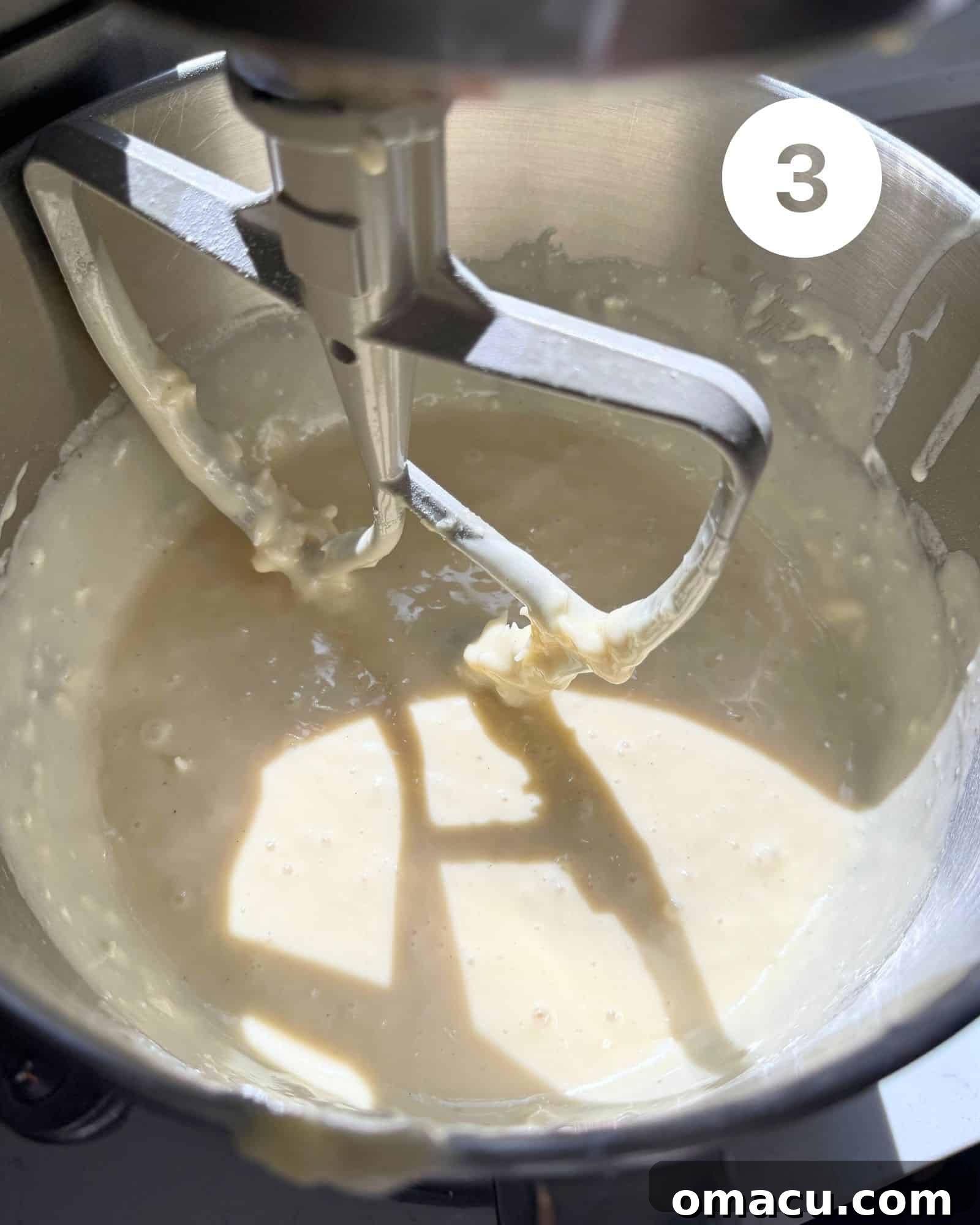 Coconut cake batter in the bowl of a stand mixer fitted with the paddle attachment, showing its creamy consistency.