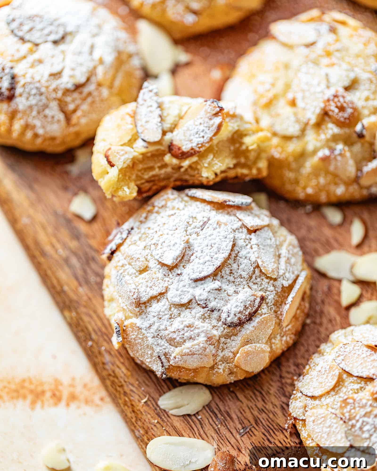 almond croissant cookies on a tray with sliced almonds and powdered sugar.