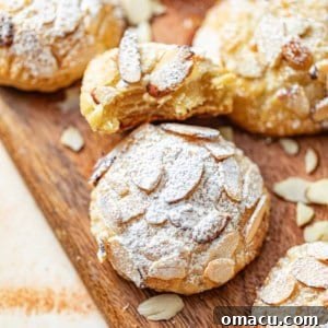 almond croissant cookies on a tray with sliced almonds and powdered sugar.