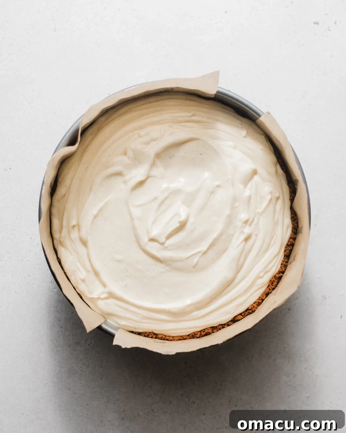 Silky cheesecake batter being poured into the prepared graham cracker crust in a springform pan.