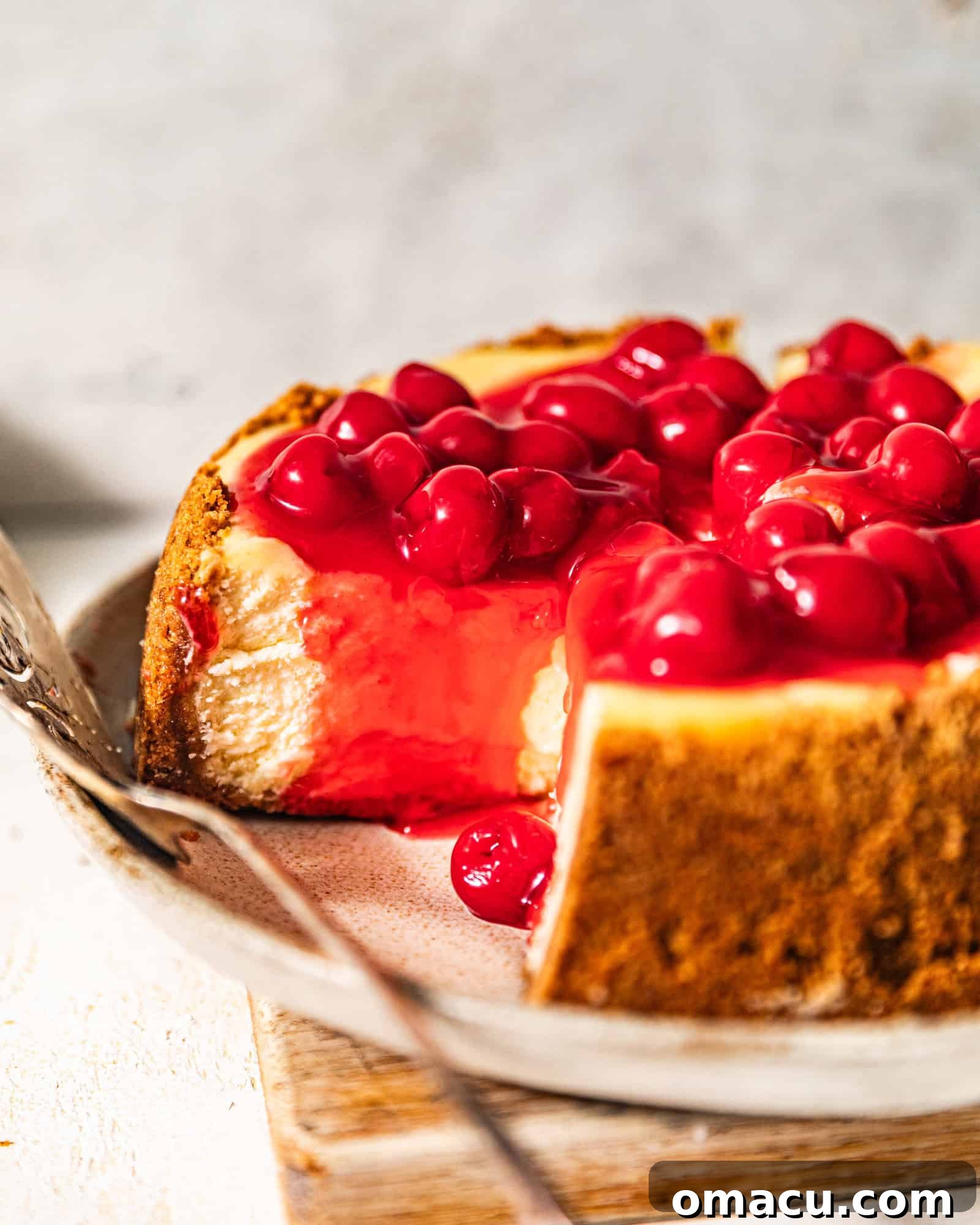 A whole cherry cheesecake on a white plate, served with a cake server, showcasing its creamy texture and vibrant topping.