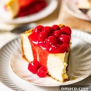 A slice of cherry cheesecake on a white plate covered in cherry pie filling.