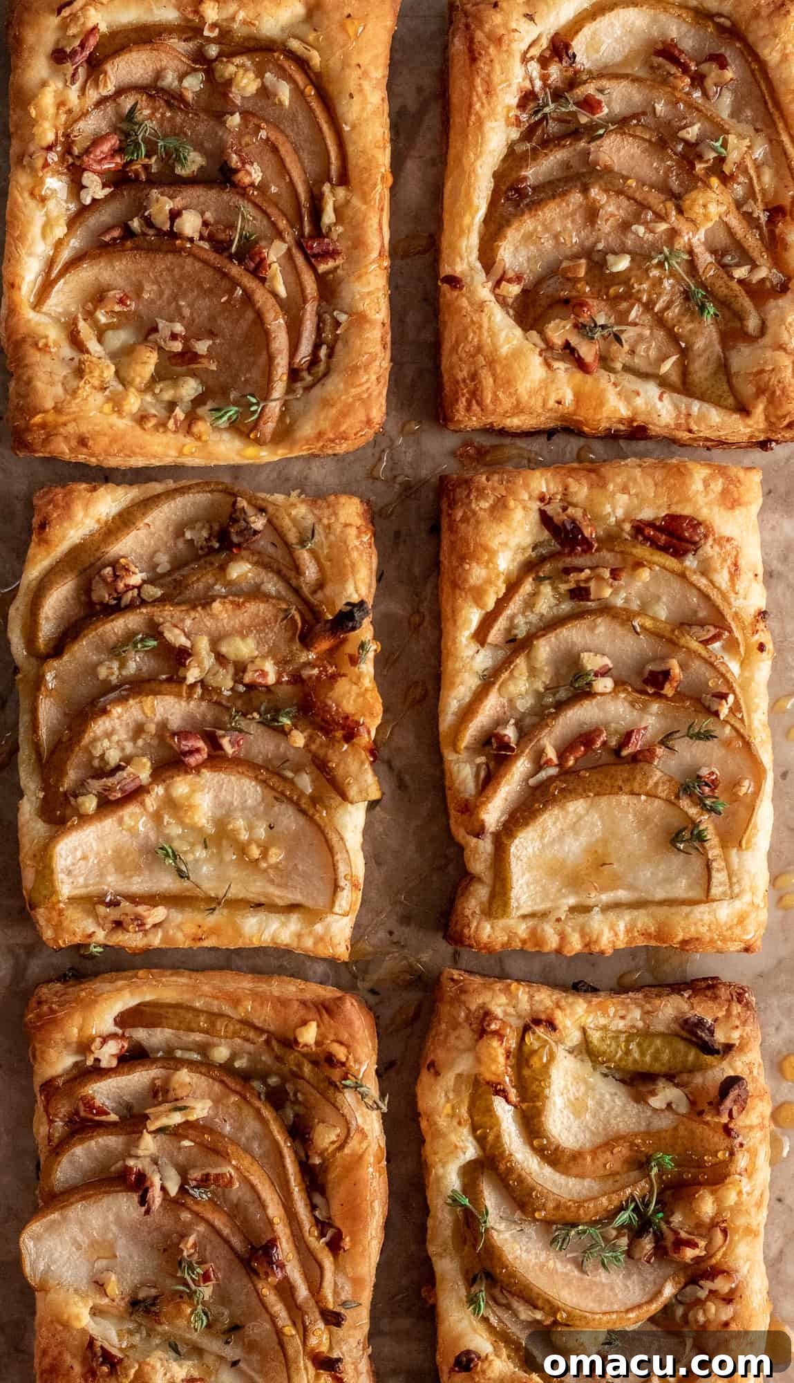 Assorted pear and gorgonzola puff pastry appetizers on a white platter, garnished with fresh thyme, ready for guests.