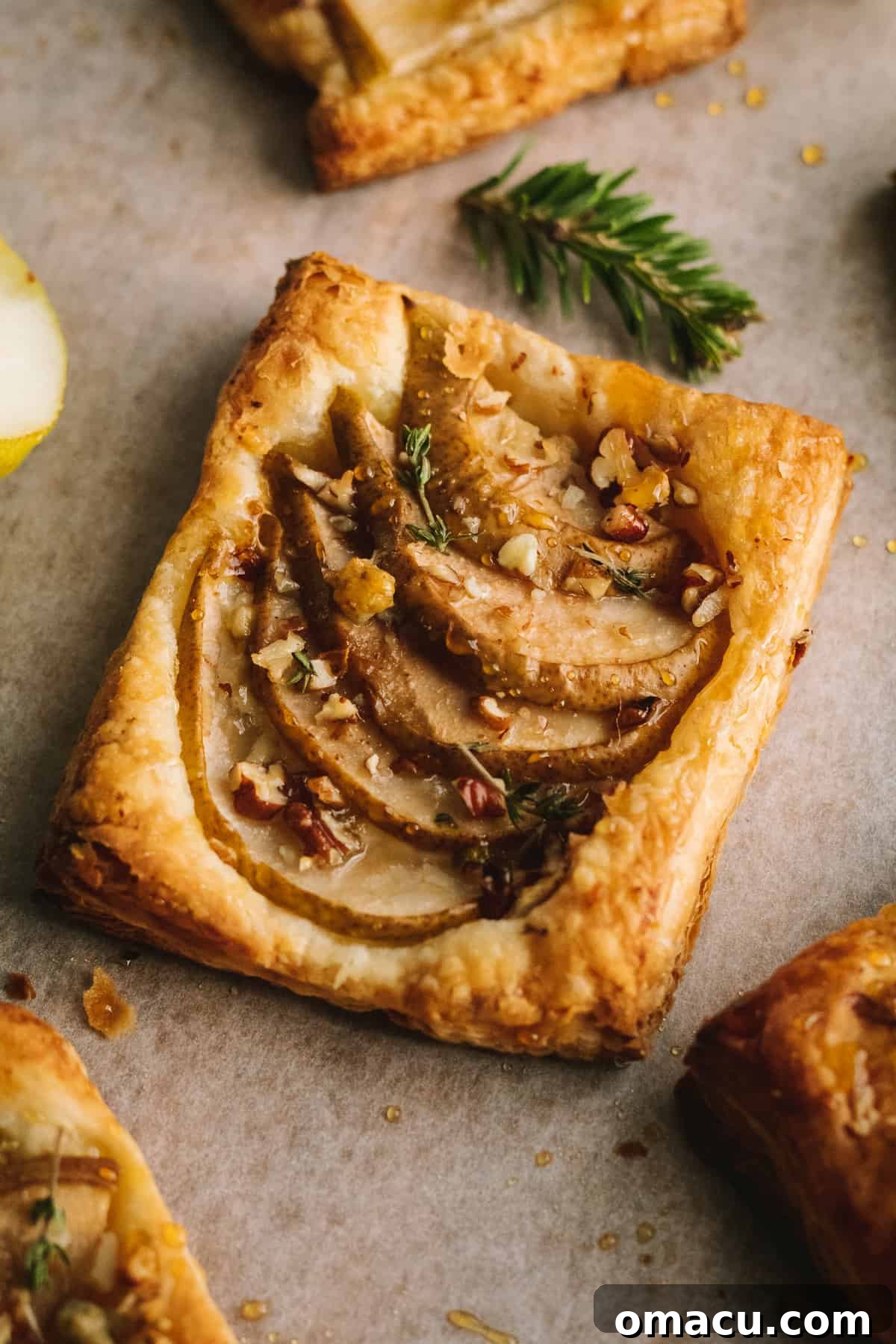 A serving of pear and gorgonzola puff pastry on a small plate, garnished with a sprig of fresh thyme.