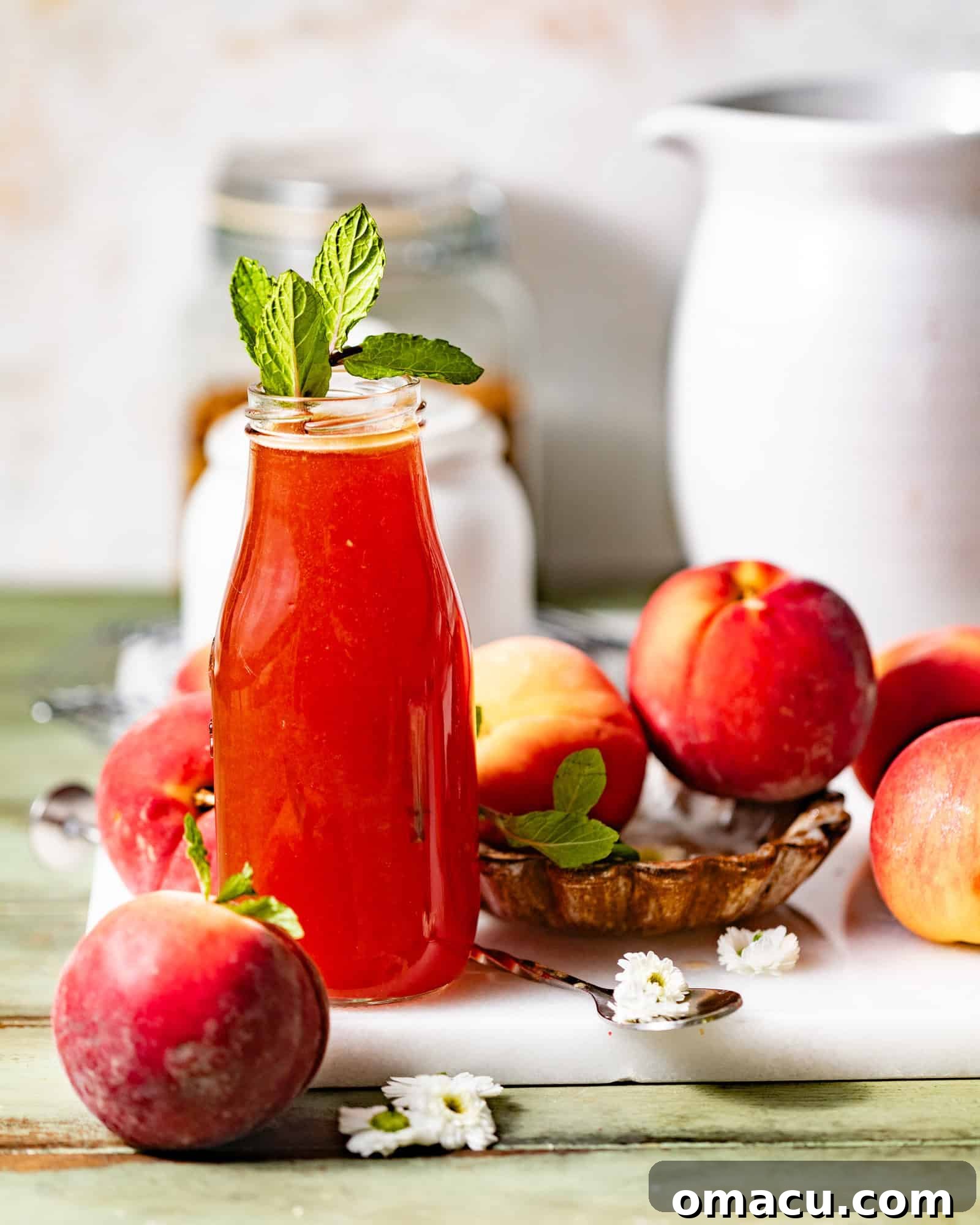 A glass bottle of homemade peach syrup, surrounded by fresh, ripe peaches and garnished with vibrant mint leaves, evoking a sense of summer freshness.