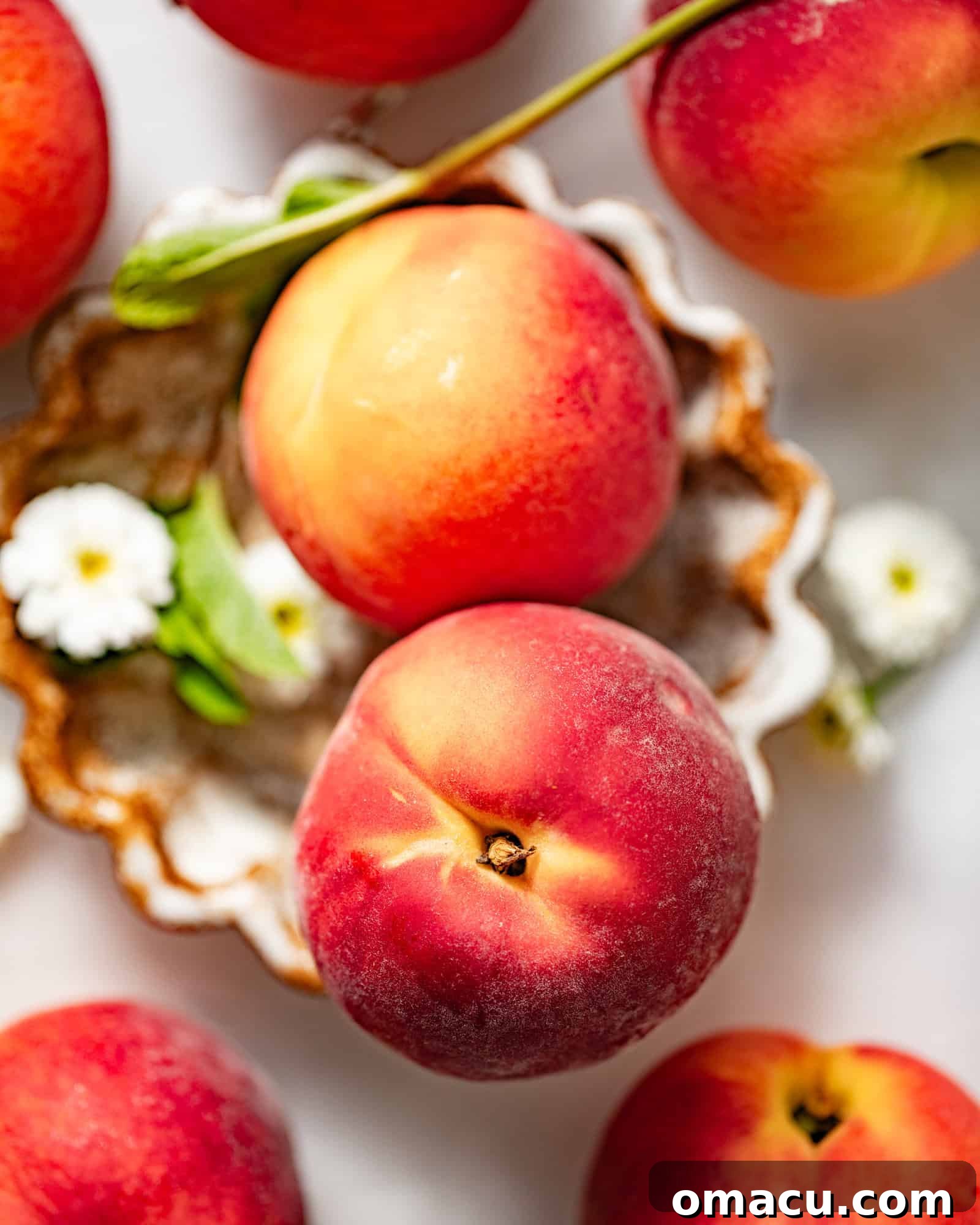 Fresh, vibrant peaches displayed beautifully on a pristine white surface, adorned with delicate white flowers, ready for making delicious syrup.