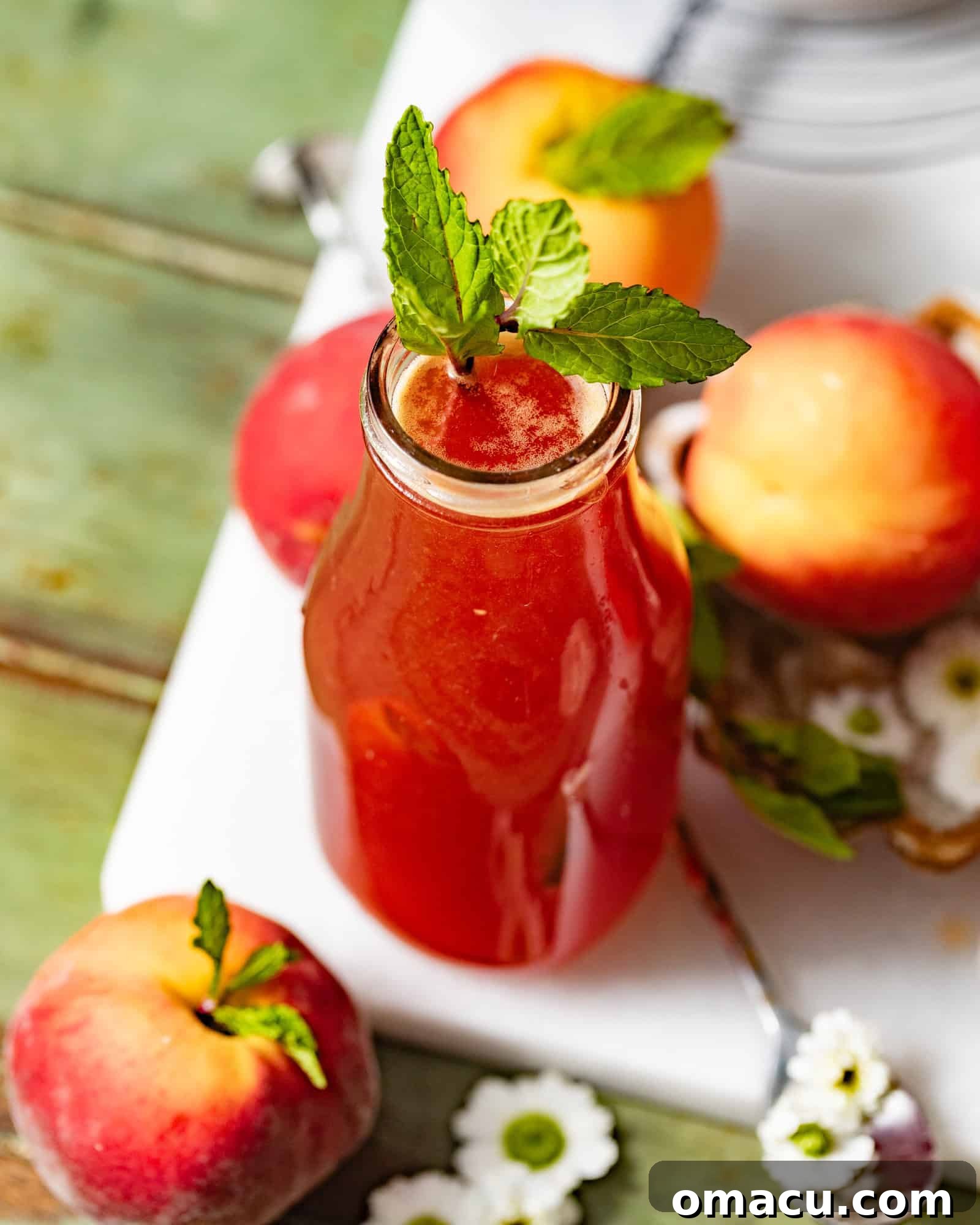 A close-up view of peach syrup in an elegant glass bottle, adorned with fresh mint, highlighting its inviting color and freshness.