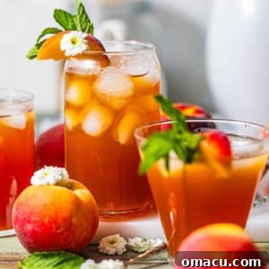 A glass of peach sweet tea with ice cubes, garnished with mint leaves, sliced peaches, and flowers, indicating a refreshing drink.