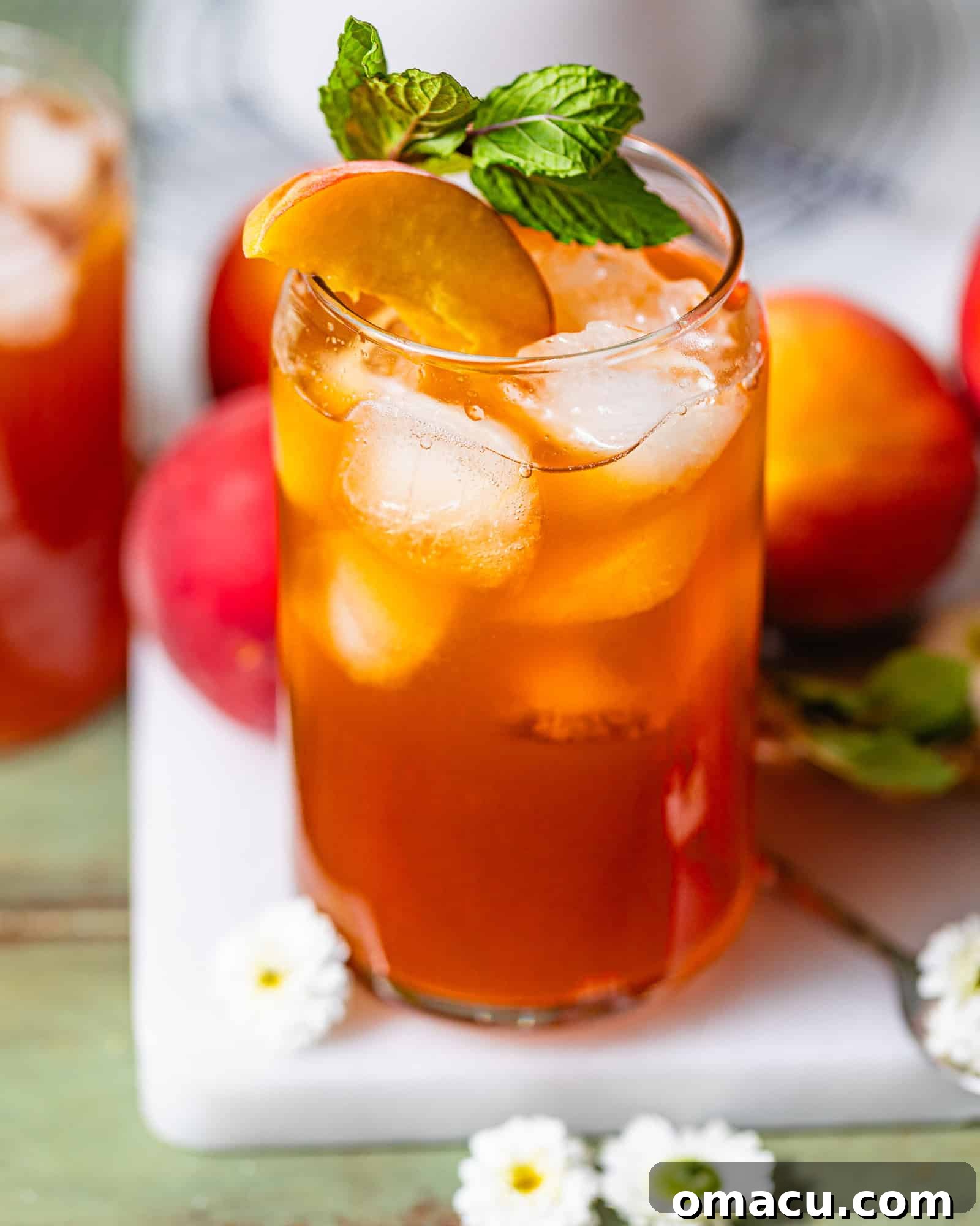 A serene shot of a glass of perfectly brewed peach sweet tea resting on a table, beautifully adorned with fresh mint leaves and whole ripe peaches, inviting a moment of refreshment.