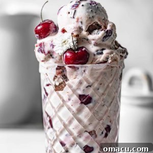 Black cherry ice cream in a glass bowl garnished with fresh cherries and edible flowers.