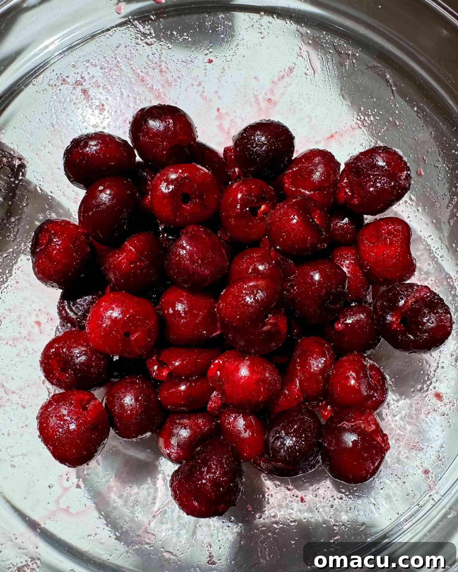 Black cherries in a large bowl coated in sugar and lemon juice.