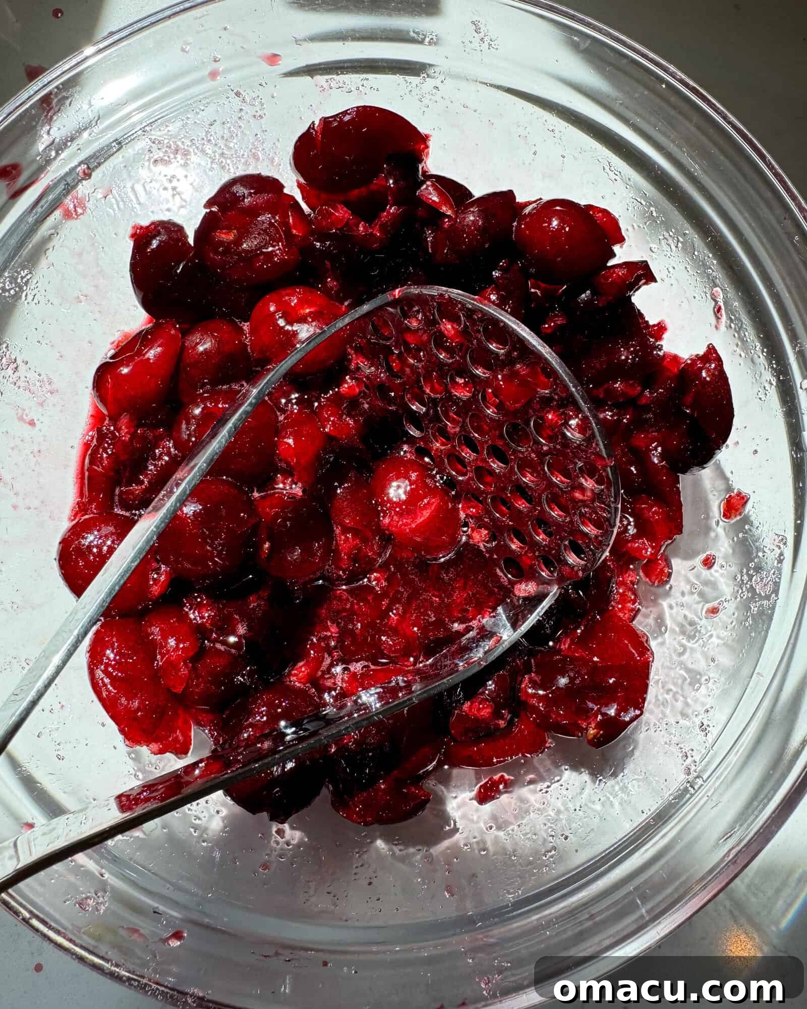 Black cherries in a large bowl mashed with a potato masher.