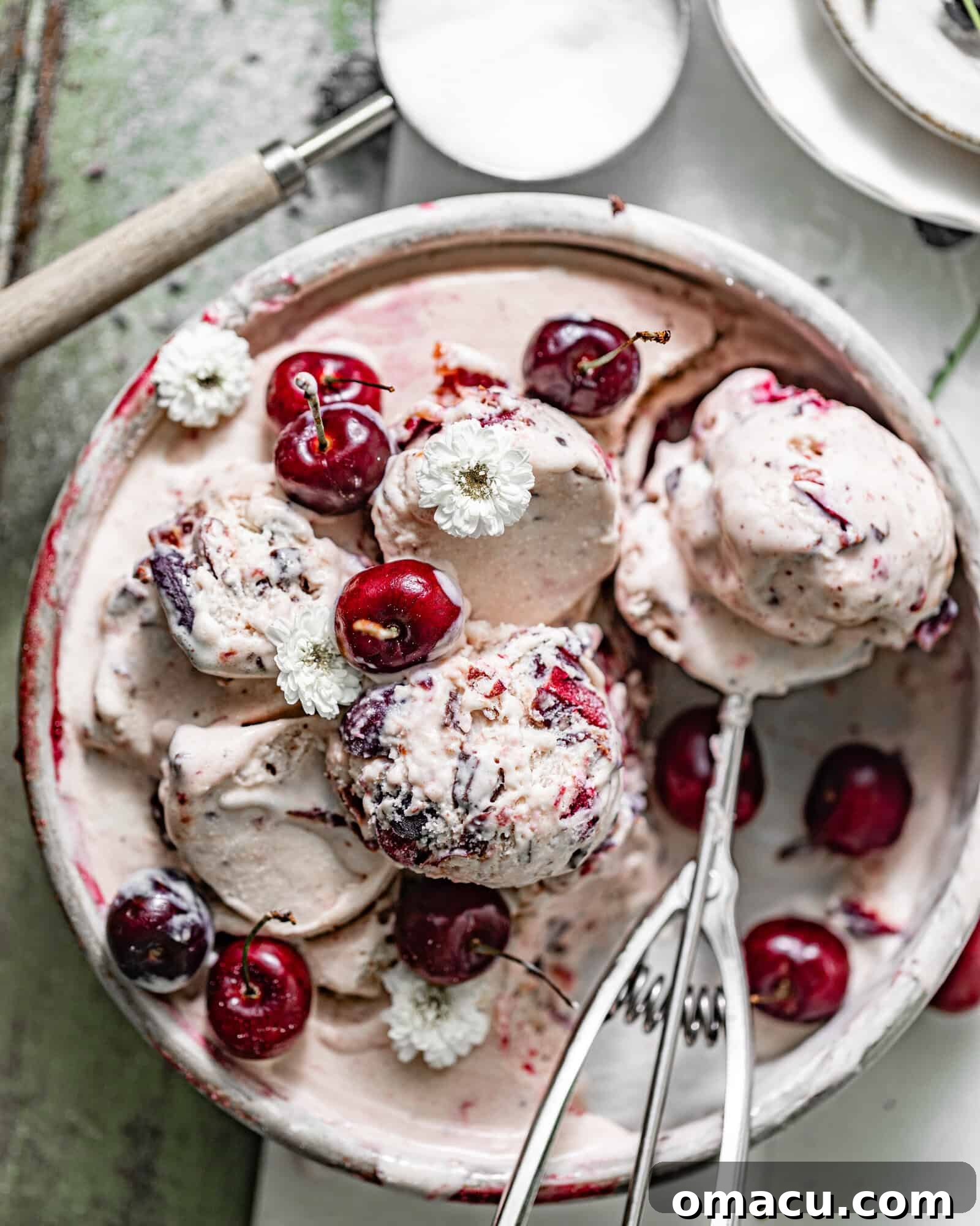 Black cherry ice cream in a metal pan with black cherries on top with an ice cream scoop.