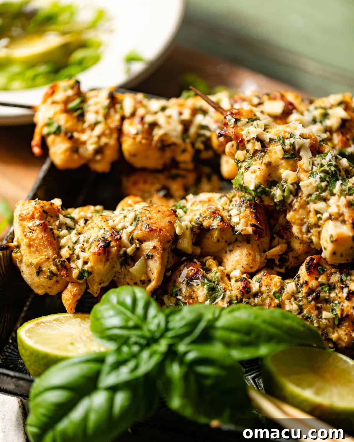 Garlic parmesan chicken skewers resting on a plate, with fresh basil leaves and lemon slices blurred in the background, ready for serving.