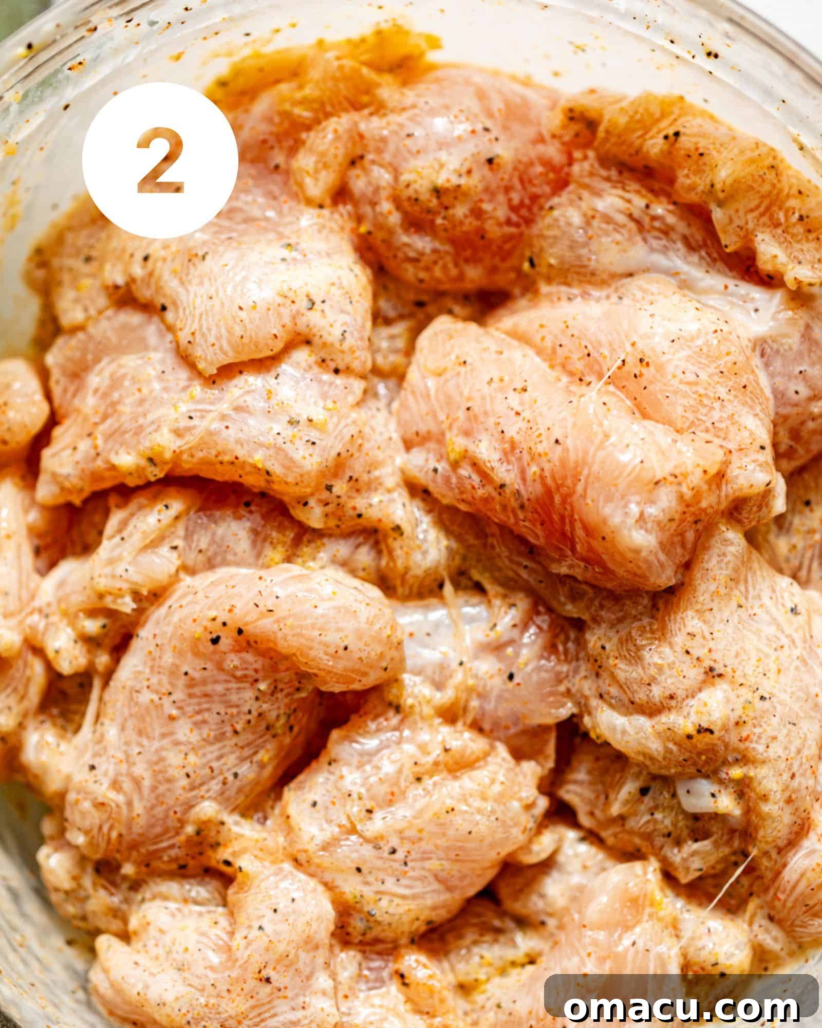 Seasoned chicken pieces glistening in a mixing bowl, ready for skewering.