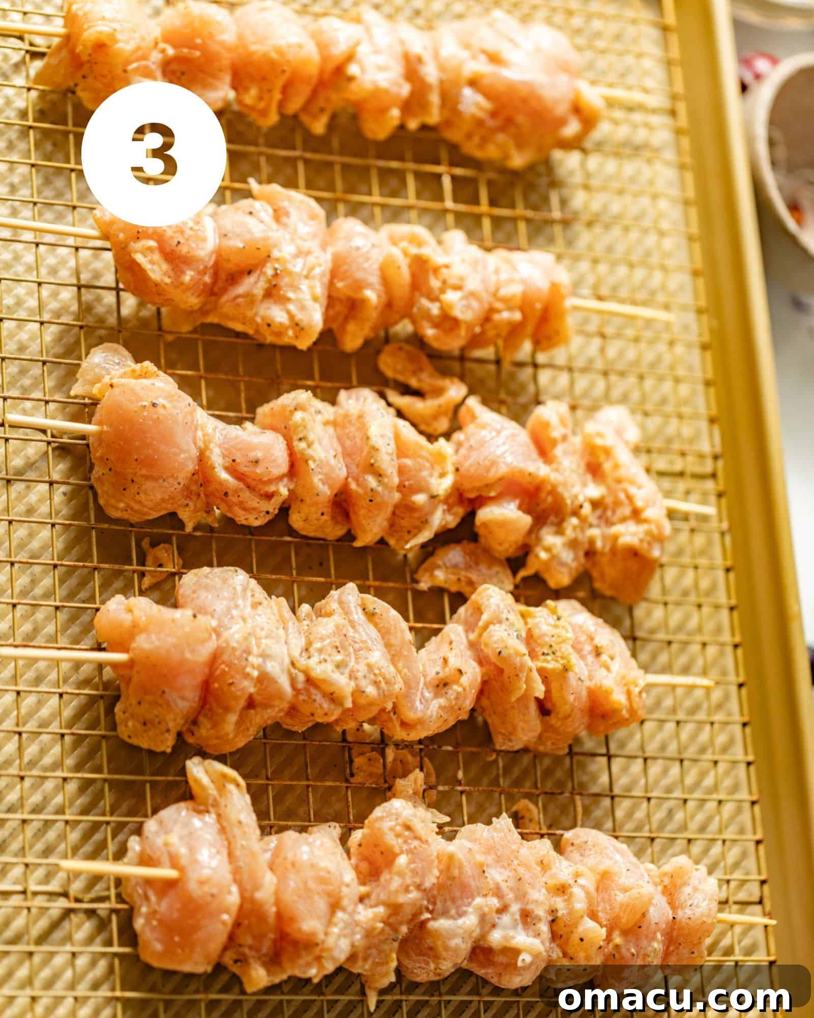 Garlic parmesan chicken skewers arranged neatly on a wire rack over a baking sheet, prepped for the oven.