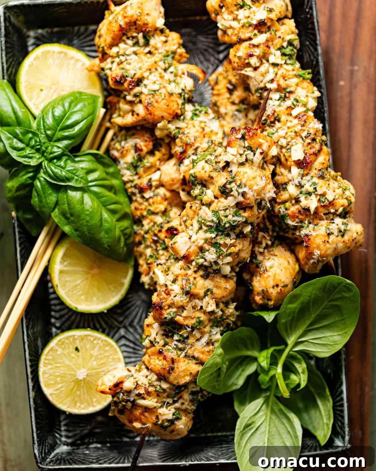 An inviting overhead view of garlic parmesan chicken skewers presented on a rustic serving board, adorned with wooden skewers, fresh herbs, and bright sliced lemons.